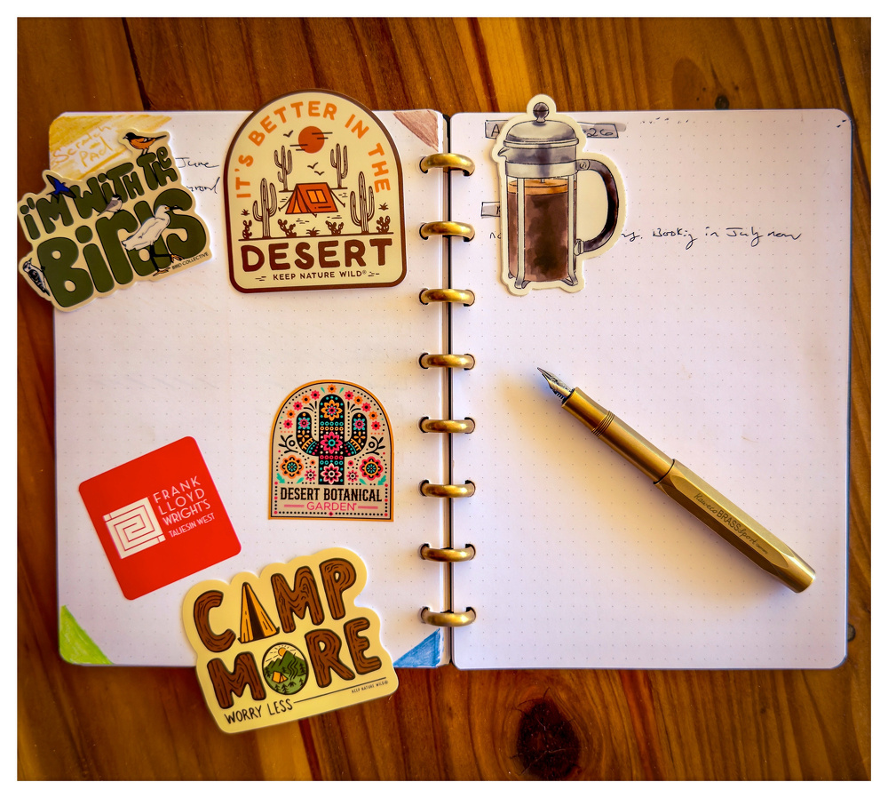 Auto-generated description: A notebook with stickers and a fountain pen is open on a wooden surface.