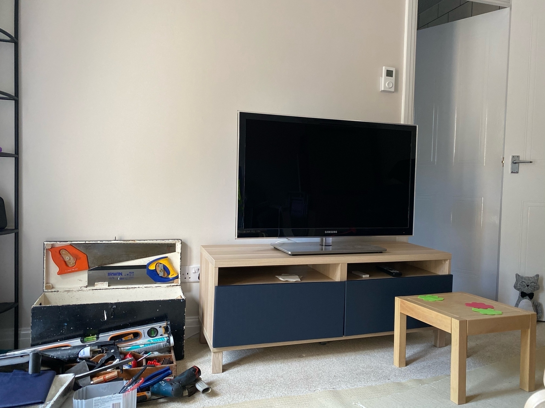 IKEA Besta TV unit with navy blue drawer fronts, TV on top. large black toolbox on the left with 2 saws in the lid. 