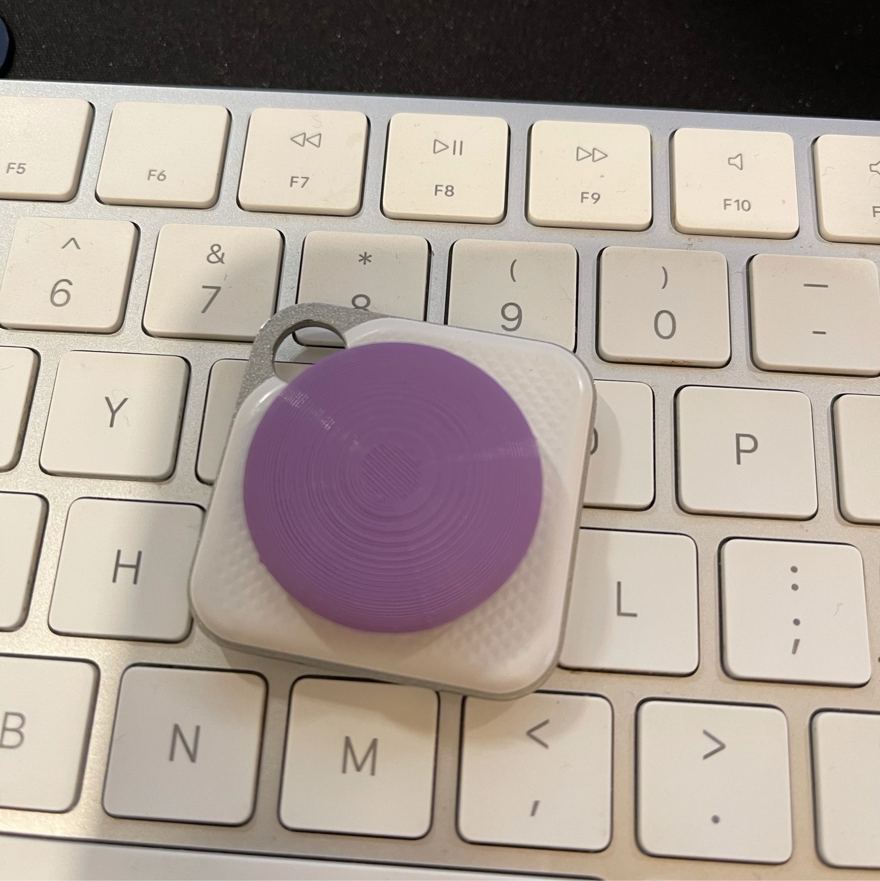 lilac "airtag" on a white Tile tracker on an apple keyboard. 