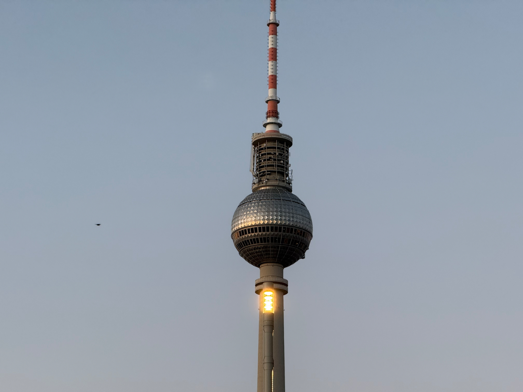 A tall tv tower with a spherical observation deck and an illuminated section stands against a clear sky.