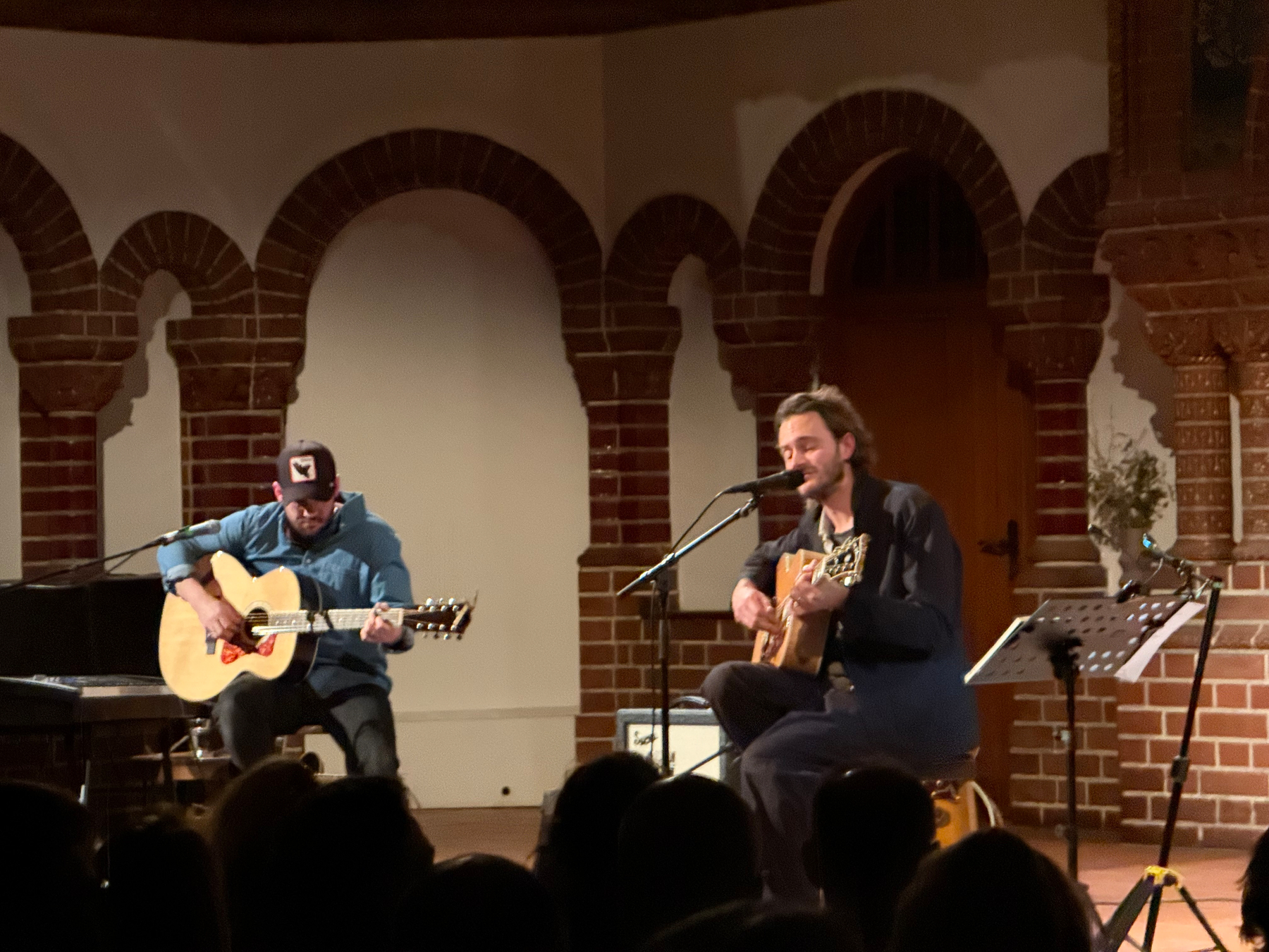 Two musicians are performing on a church altar with acoustic guitars in a warm light.