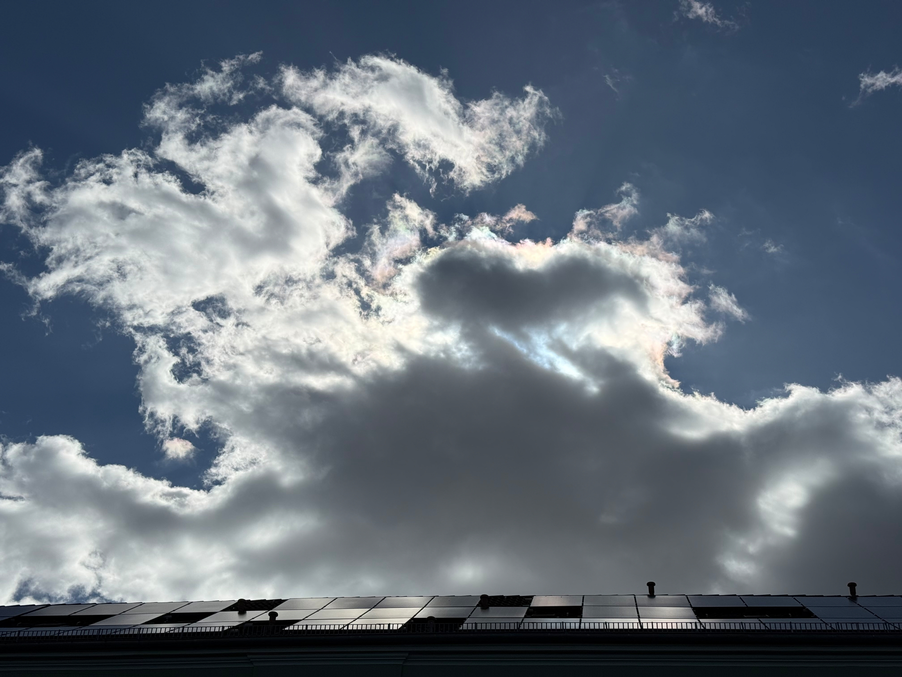 Clouds partially obscure the sun in a blue sky above a row of solar panels.