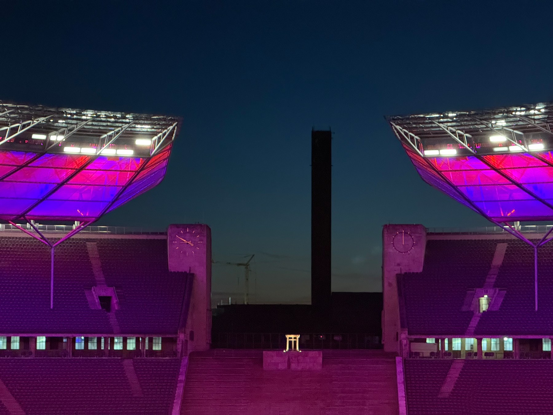 A stadium at dusk with illuminated roof structures and a central tower in the background.