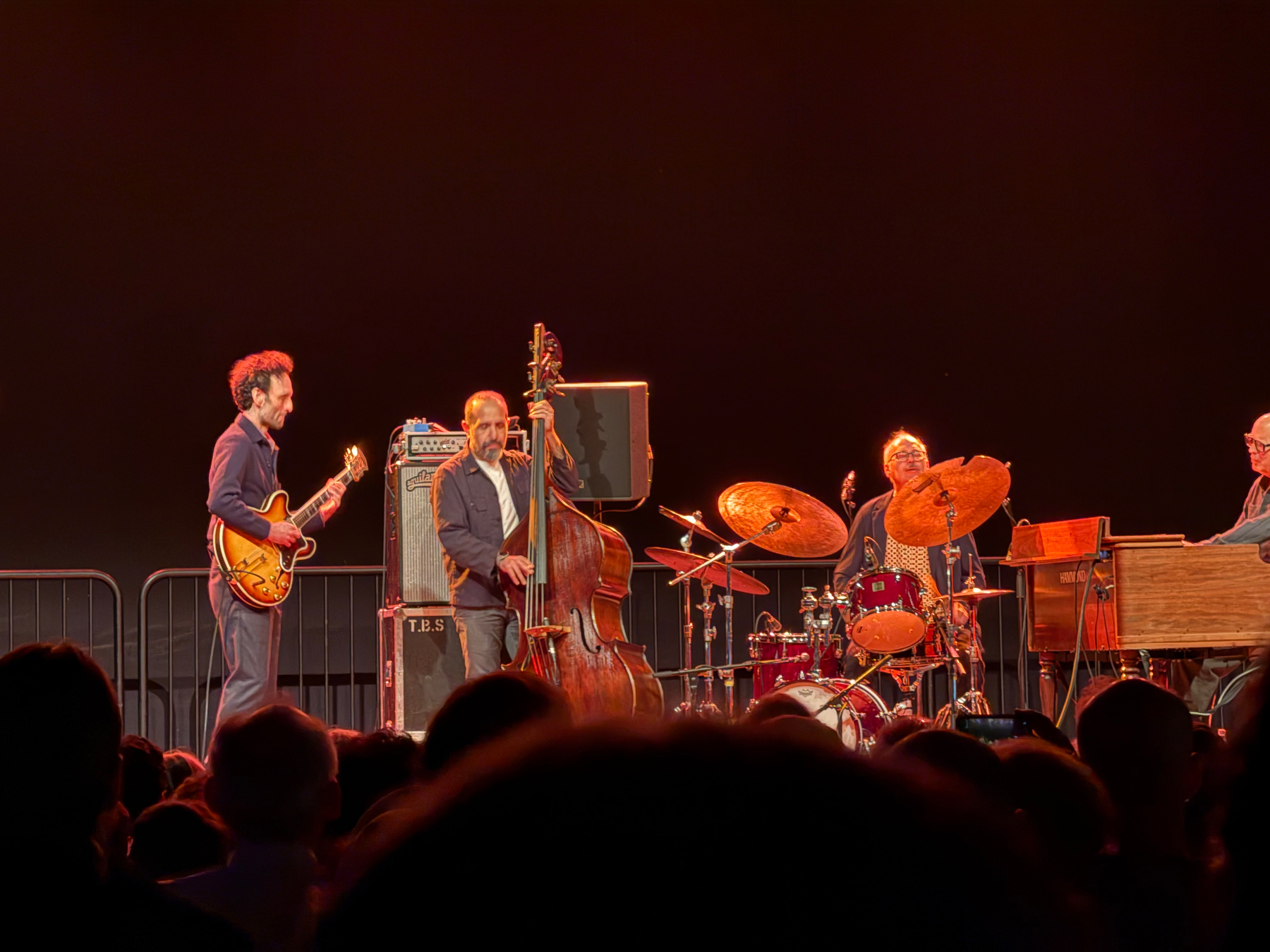 A live jazz band performs on stage with a guitarist, double bassist, drummer, and an organ player.