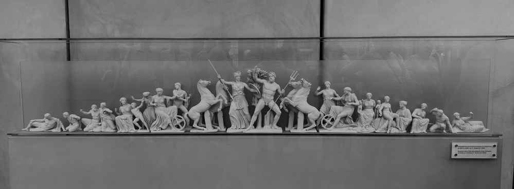 A detailed display of a classical relief sculpture depicts a dynamic battle scene with multiple human and mythical figures engaged in combat.