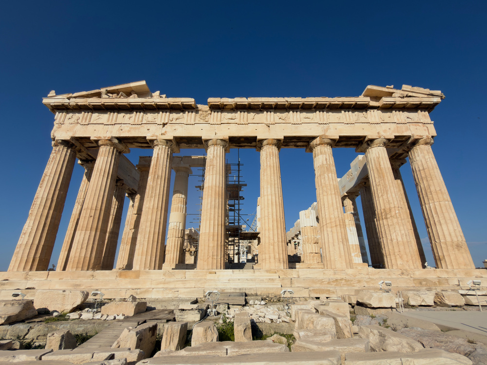 A view of the Parthenon, an ancient Greek temple with Doric columns, set against a clear blue sky.