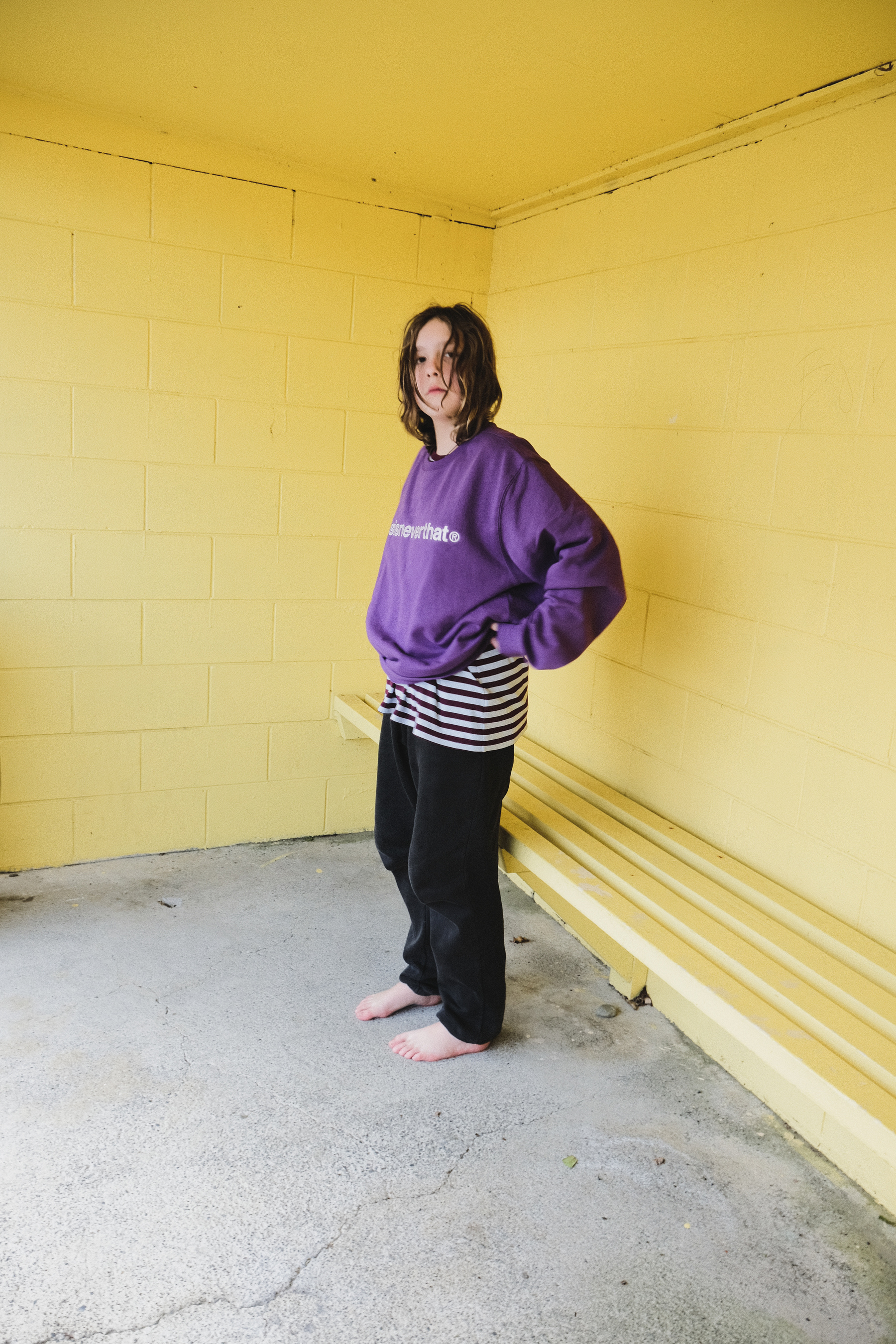 A girl putting on a purple sweatshirt in a yellow bus shelter. 