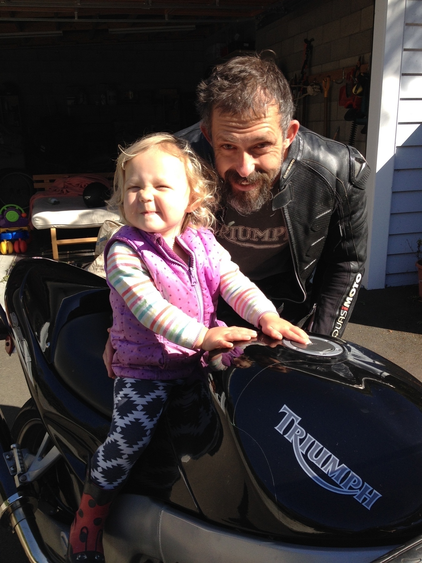 A little girl is excited to be on a triumph sprint RS while her dad stands beside her smiling