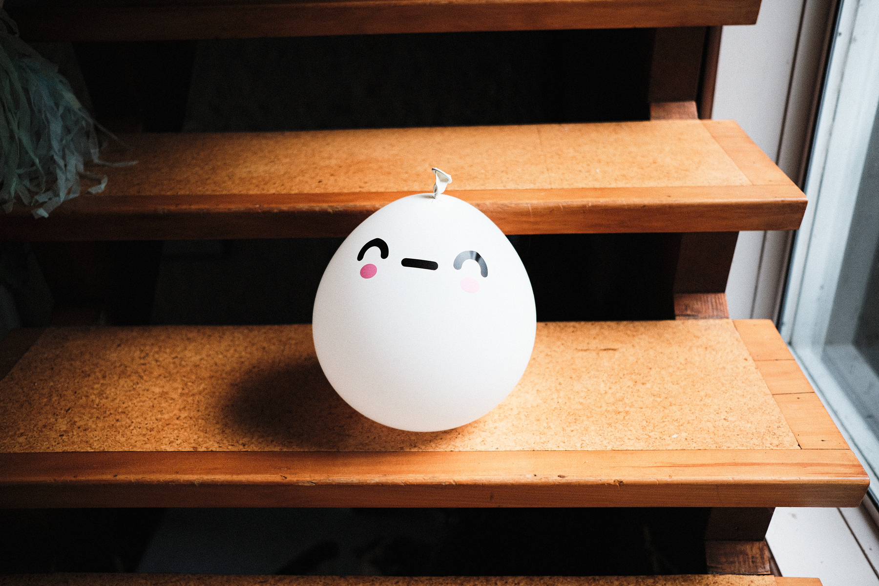 A balloon with a kawaii face on it, sitting on some wooden stairs