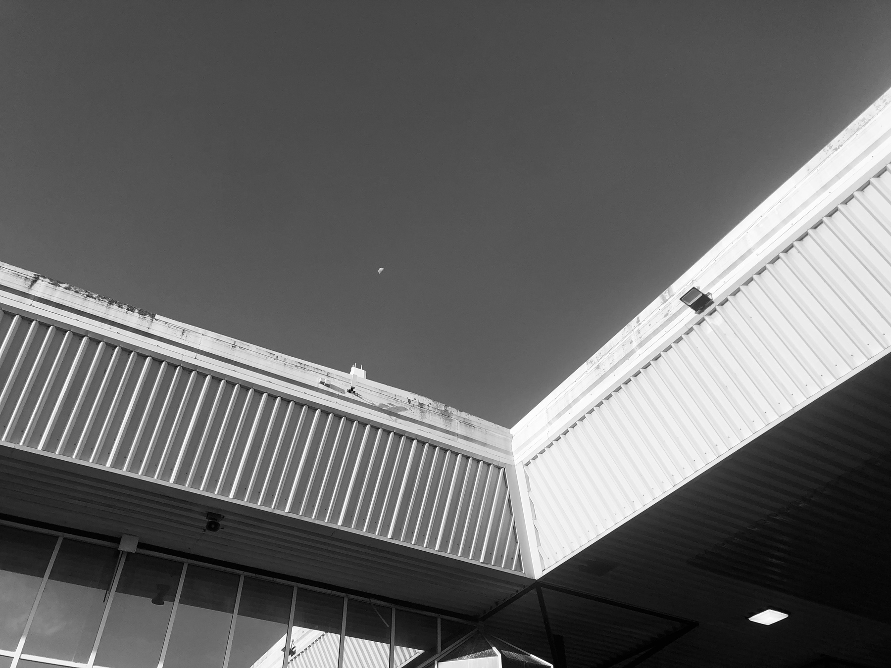 Black and white photo of the roof of a train station. A sliver of moon is just visible. 