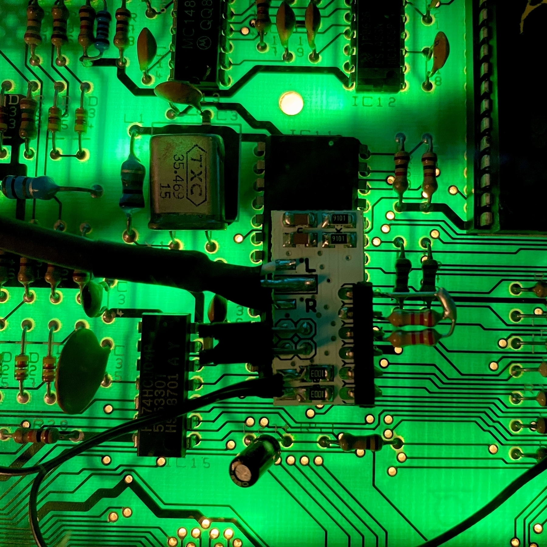 Close up photo of a back-lit printed circuit board. In the centre of the image a white adapter-board with very small components has been attached on top of a large microchip. Various wires are coming off the adaptor and out of sight.