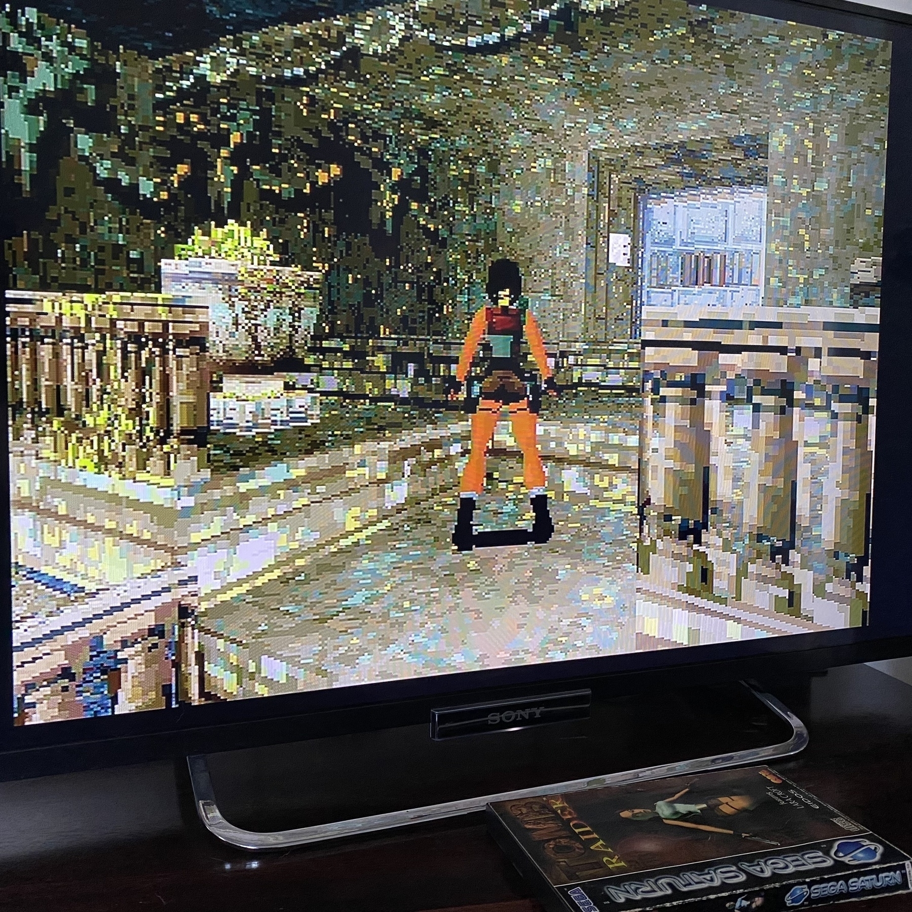Screenshot of PAL version of Tomb Raider, the Cistern level. Lara Croft is standing on a stone balcony looking at a disguised moveable block that’s hiding a secret area. The texture of the block is slightly different to the surrounding walls.