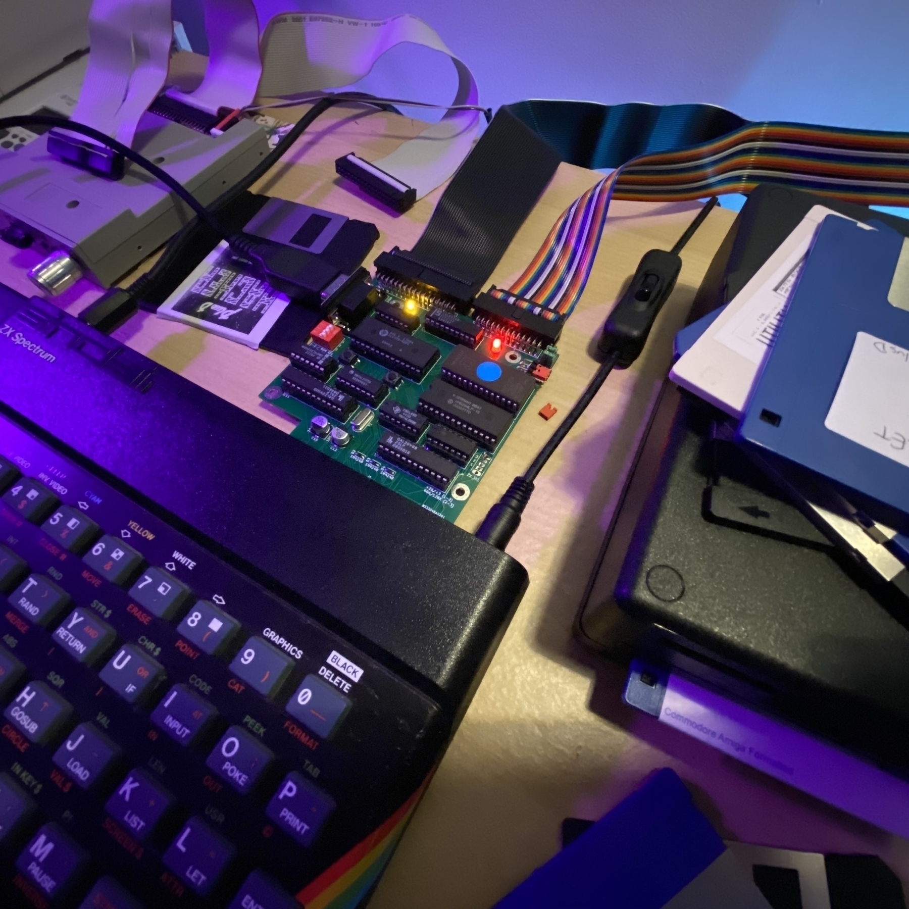 PlusD interface connected to a 48K ZX Spectrum. Floppy disks, drives and ribbon cables are strewn around. Yellow and red LEDs are brightly glowing on the PlusD. It has no casing, so the circuit board is visible.