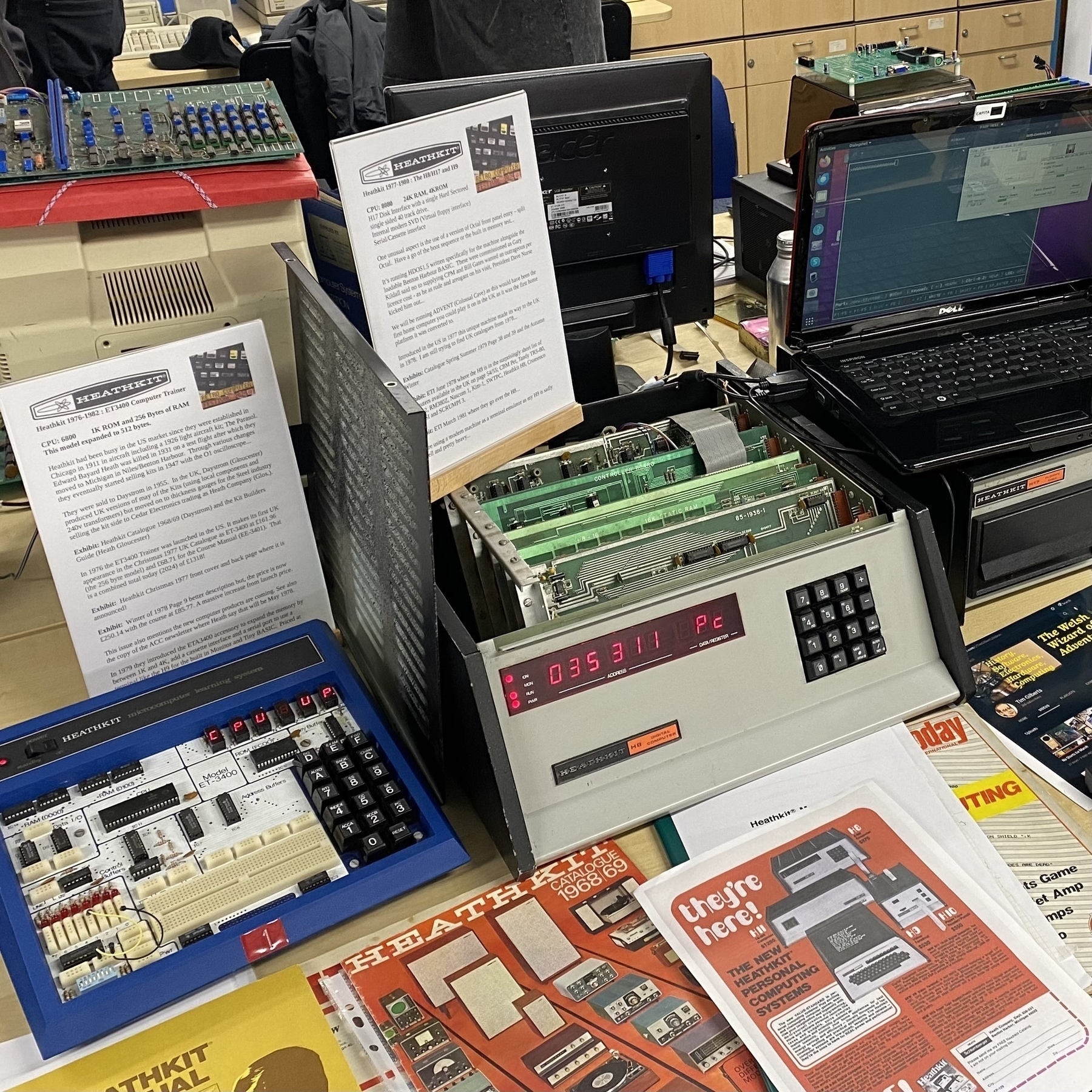 A display of Heathkit computers magazines and catalogs from the late 70s. The machines are operating, with their numerical displays glowing.