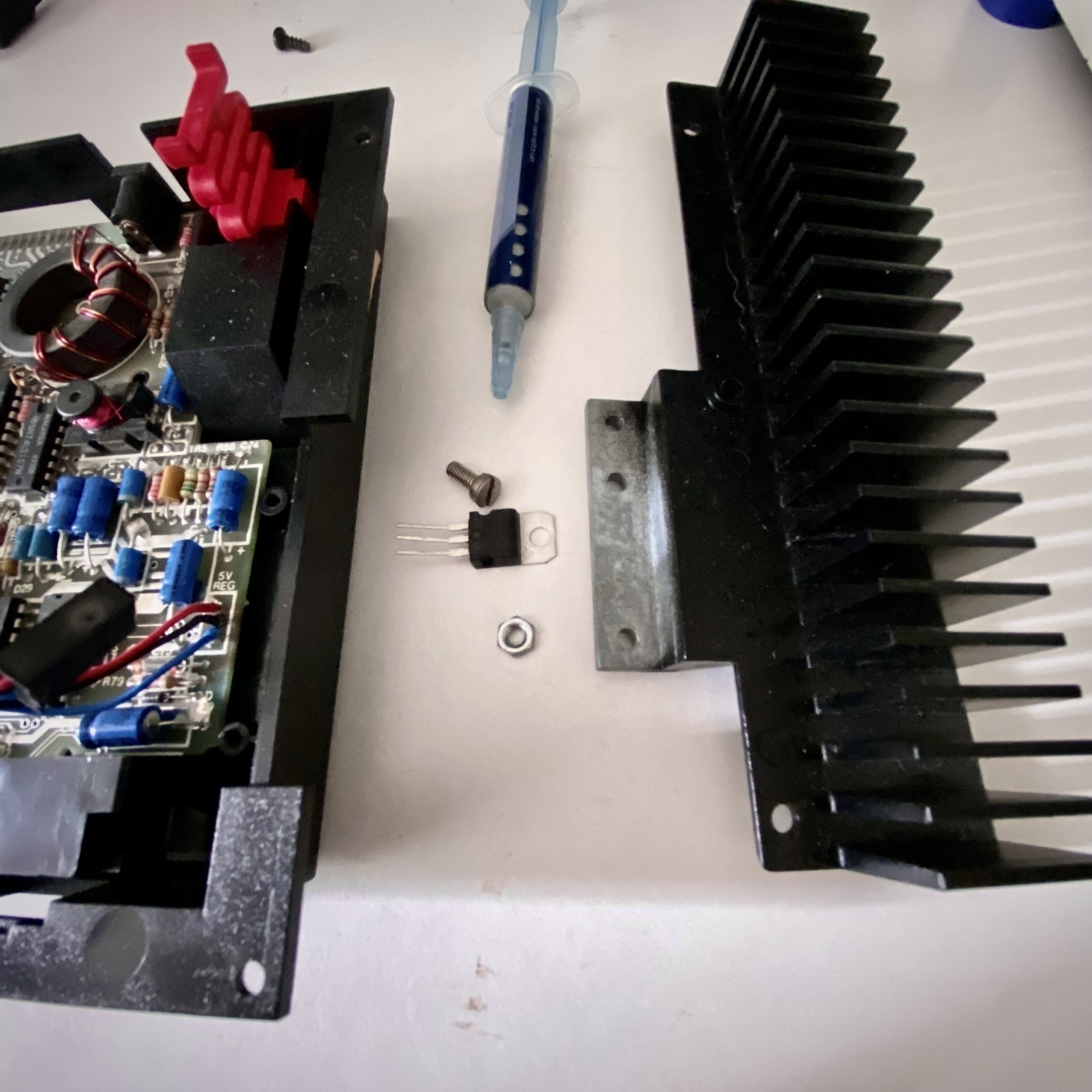 Disassembled ZX Spectrum+ 128. The iconic finned radiator heatsink has been detached, as has the voltage regulator. Also pictured is a syringe of thermal compound normally used on PC CPUs or GPUs or whatever.