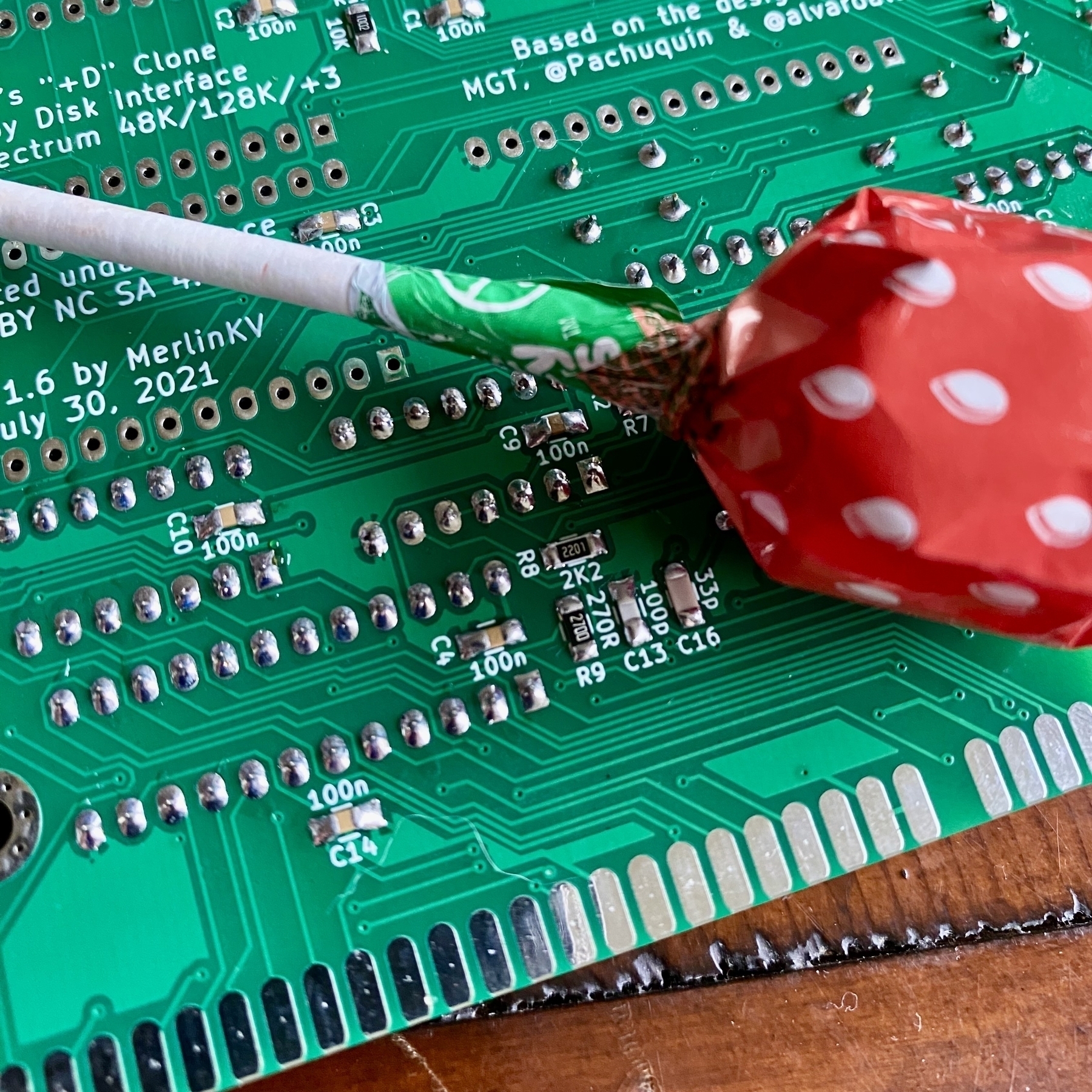 Detail of a partially assembled circuit board. Small SMT components on millimetres in size have been soldered to the board. A strawberry Chuppa Chupp lolly has been put into the photograph to give a sense of scale.