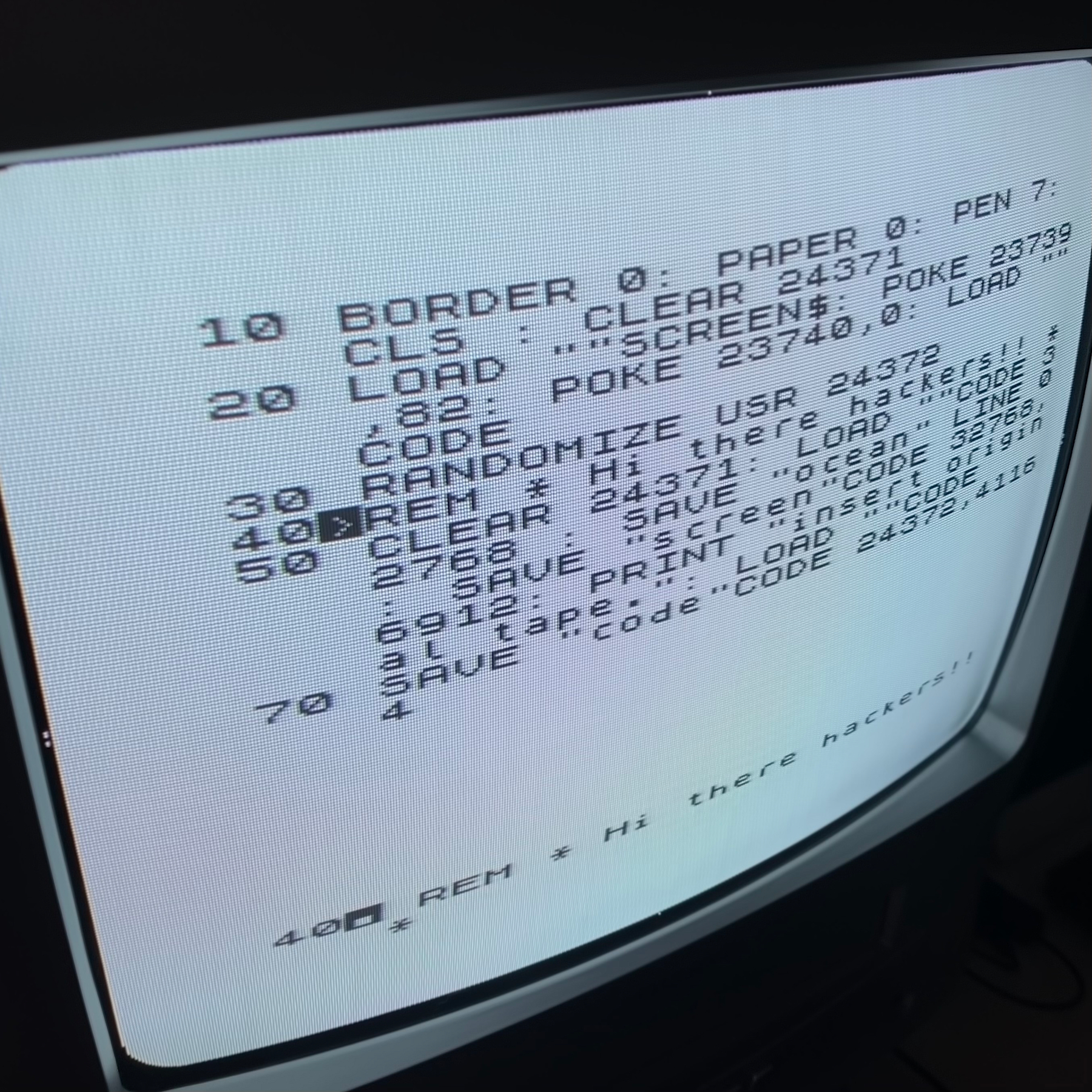 BASIC program listing on a TV screen. The highlight line is a REMark statement that reads, “Hi there hackers!!”