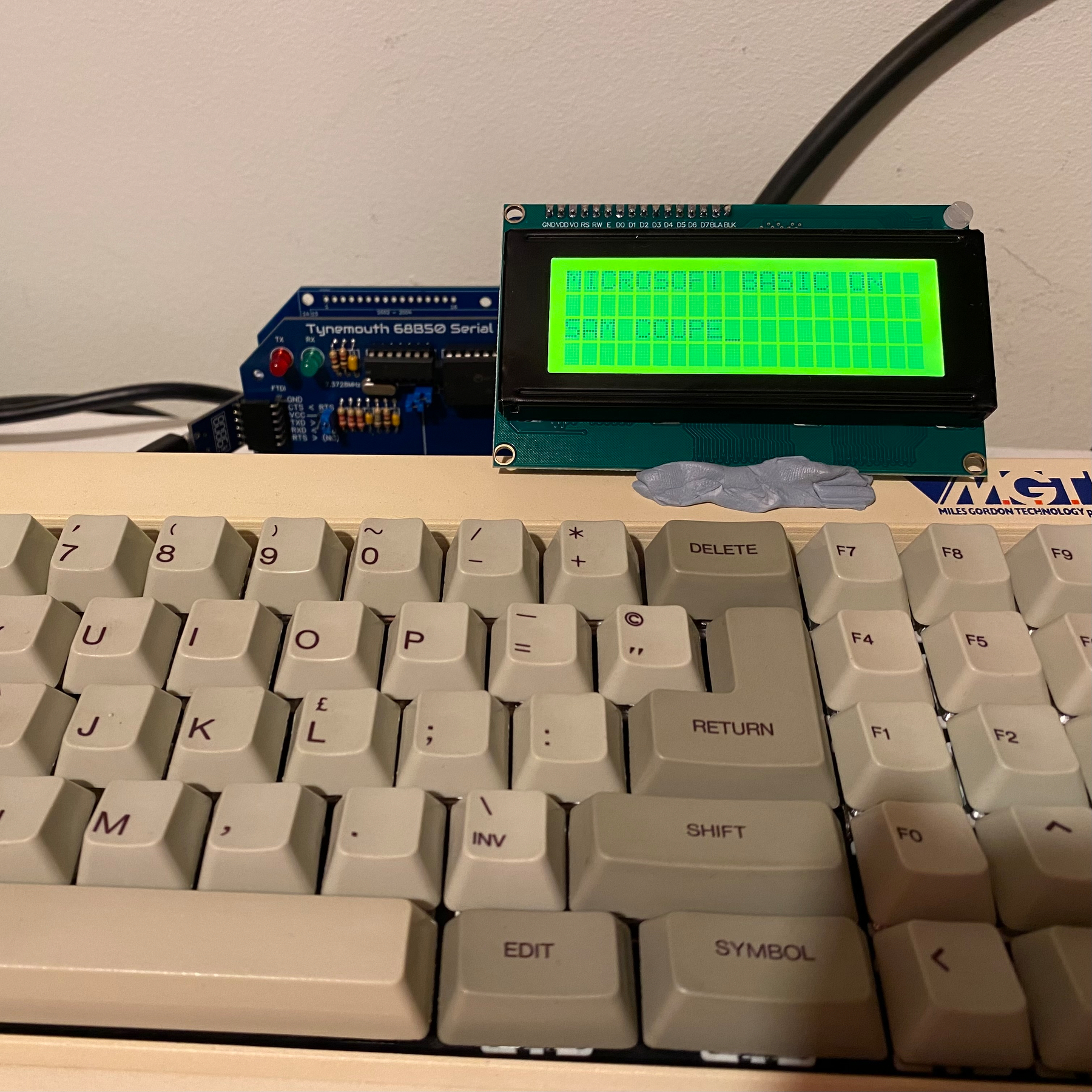 Closeup picture of SAM Coupé with serial interface and LCD attached. Text on the display reads “MICROSOFT BASIC ON SAM COUPE”.