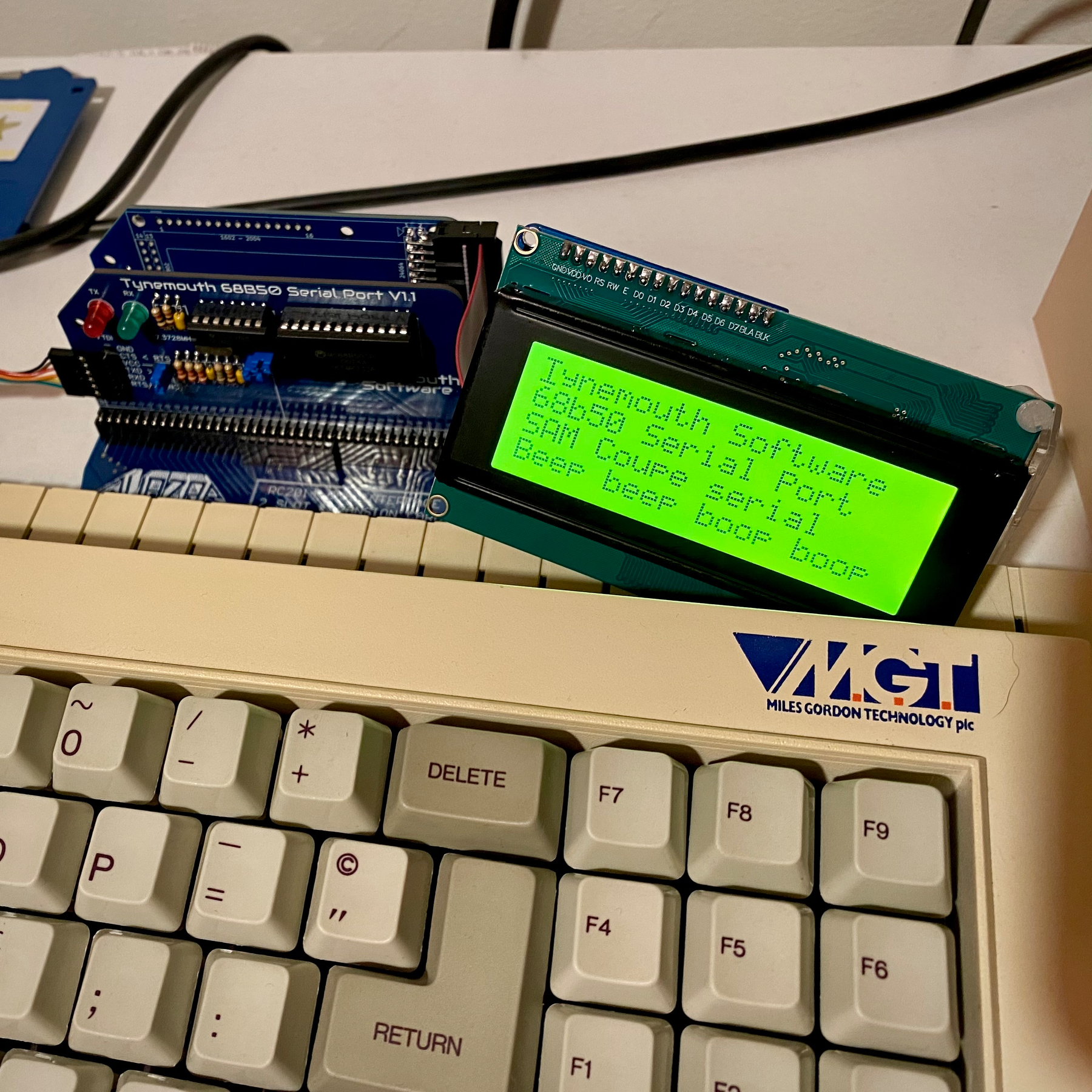 Closeup of a SAM Coupé computer with an LCD screen attached and a serial interface. Text on the display reads “Tynemouth Software 68b50 Serial Port. SAM Coupe serial. Beep beep boop boop”