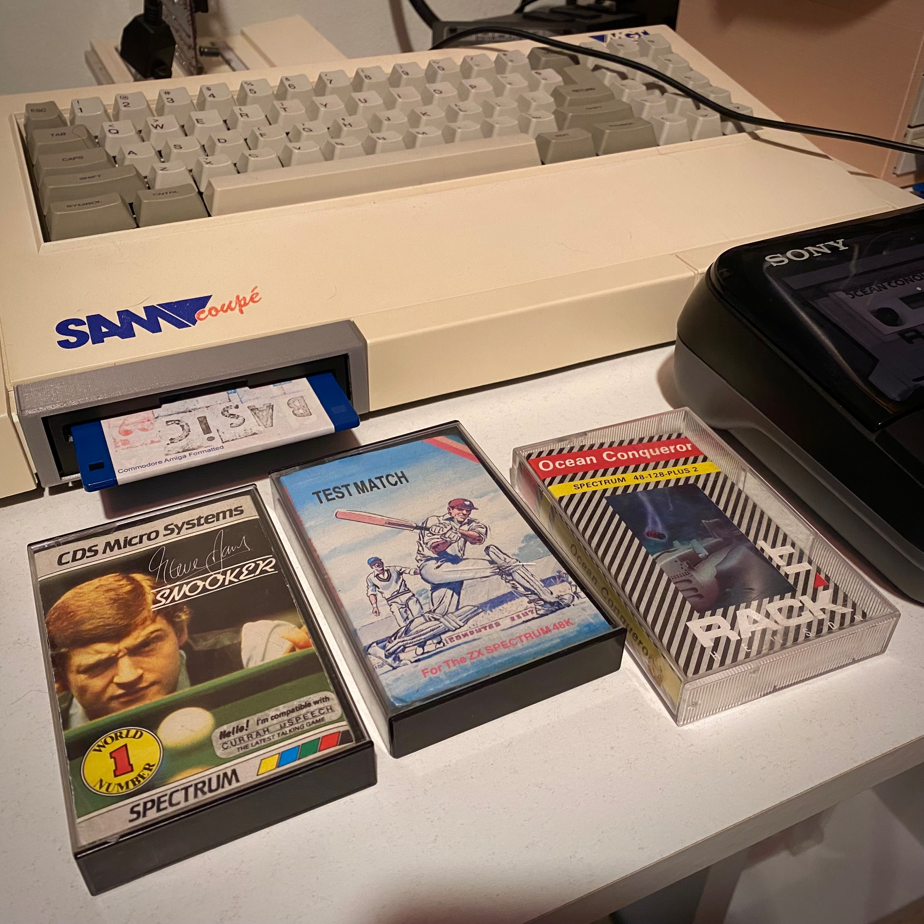 A photograph of a SAM Coupé computer and some ZX Spectrum software cassette boxes. Titles read “Steve Davis Snooker”, “Test Match” and “Ocean Conqueror”. 