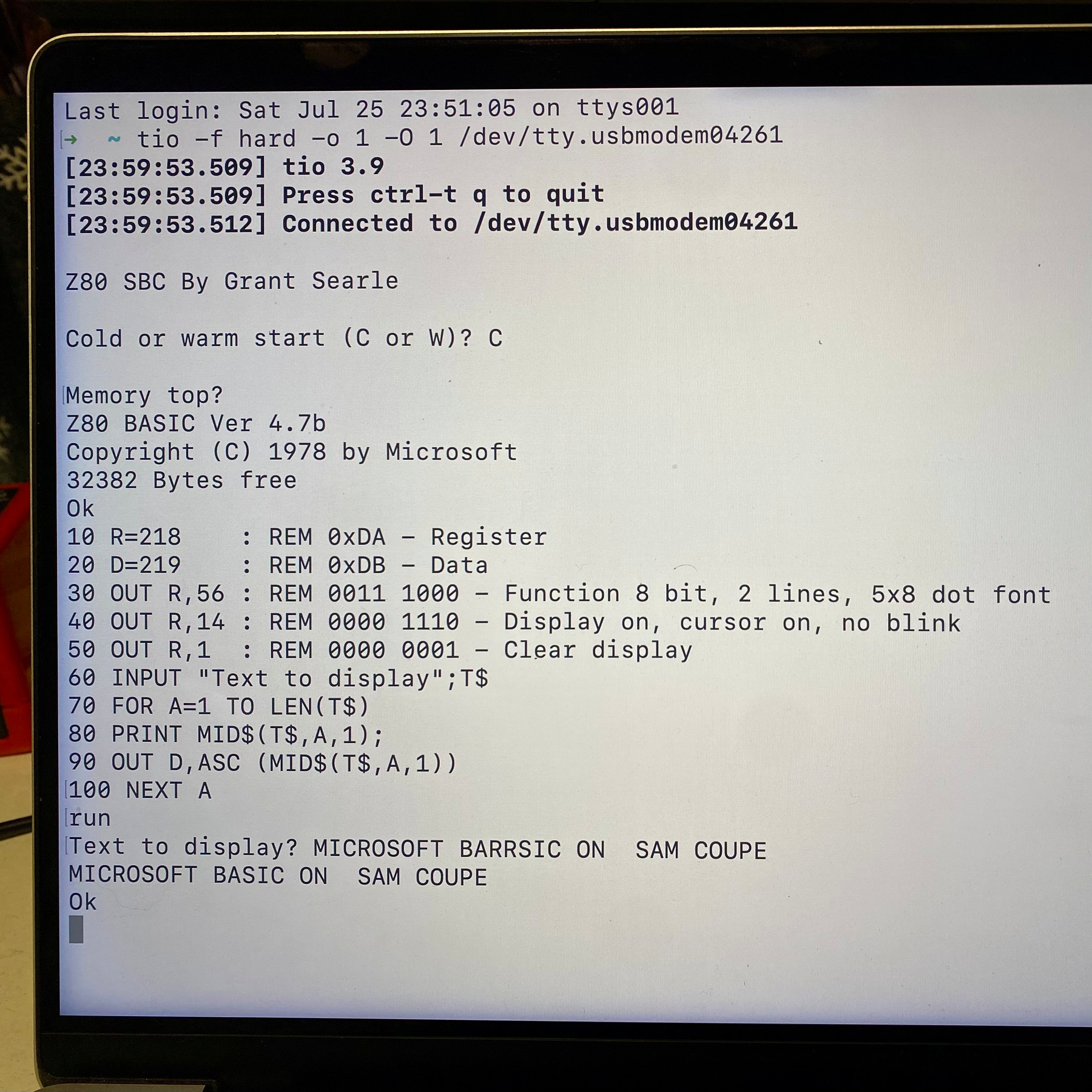 Photograph of a laptop screen. The running program is a terminal, running Tio serial terminal emulator. The information listed shows we are connected to USB serial, and the output is being generated by SAM. Microsoft BASIC is starting up and we’ve typed in a short program. The program accepts user input and displays it on the attached LCD.
