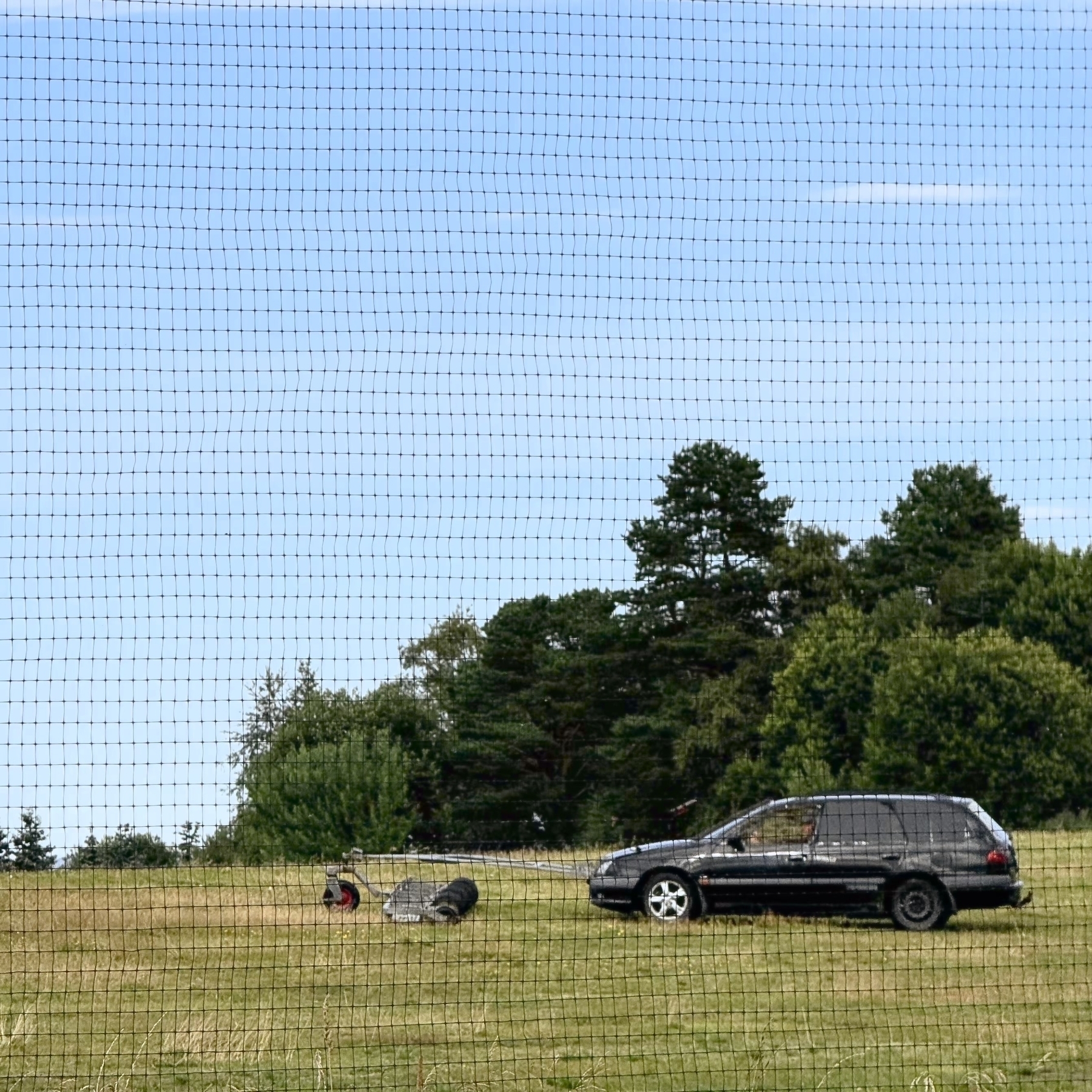 A person is collecting the golfballs from the driving range with a black car.