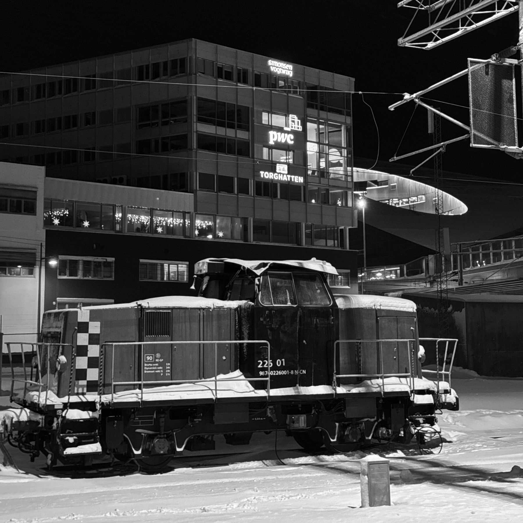 A snow-covered train engine sits on a snowy track at night, with a modern building illuminated in the background.