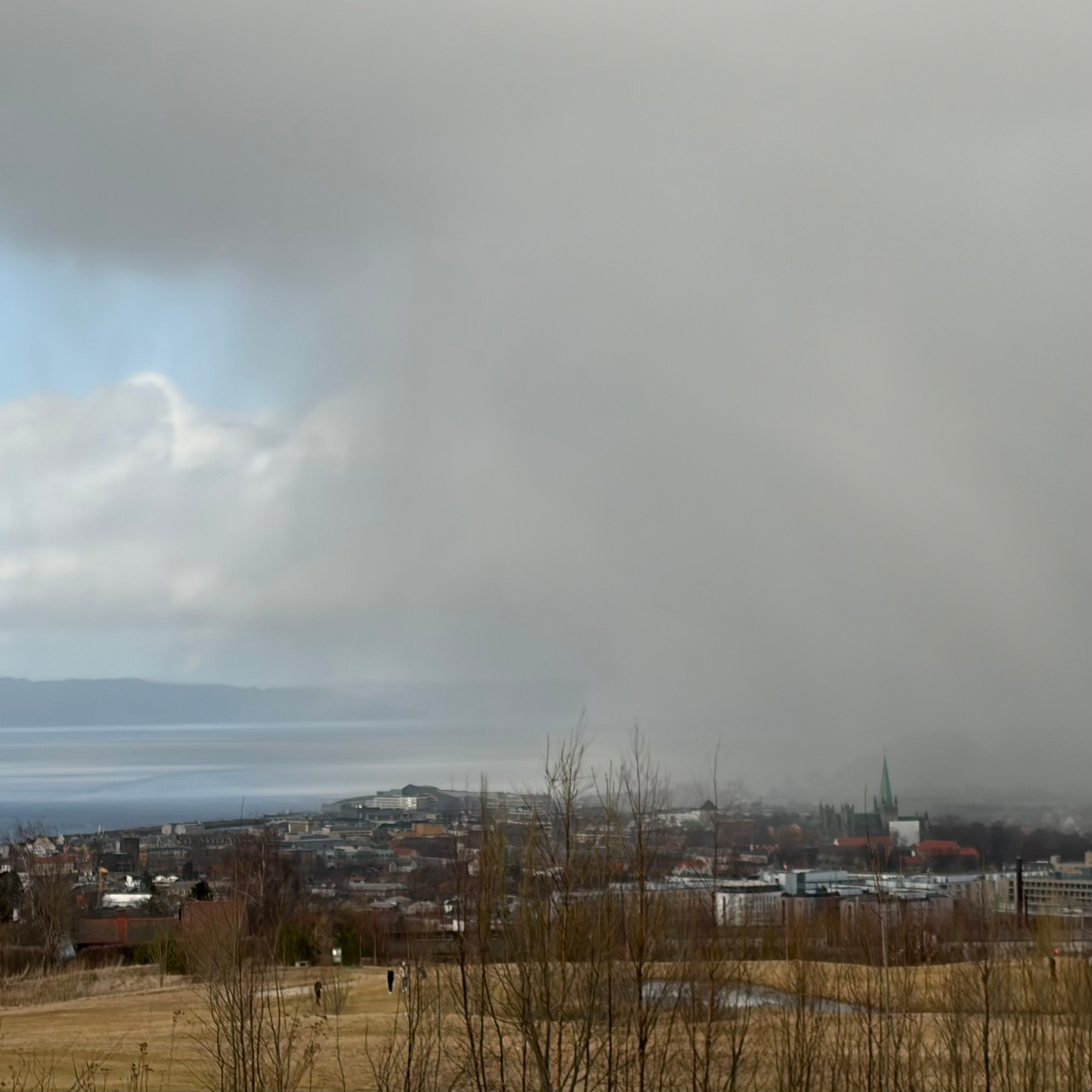 Et bylandskap ses under en skyet himmel med lavt hengende skyer og svak tåke som svever nær bakken.