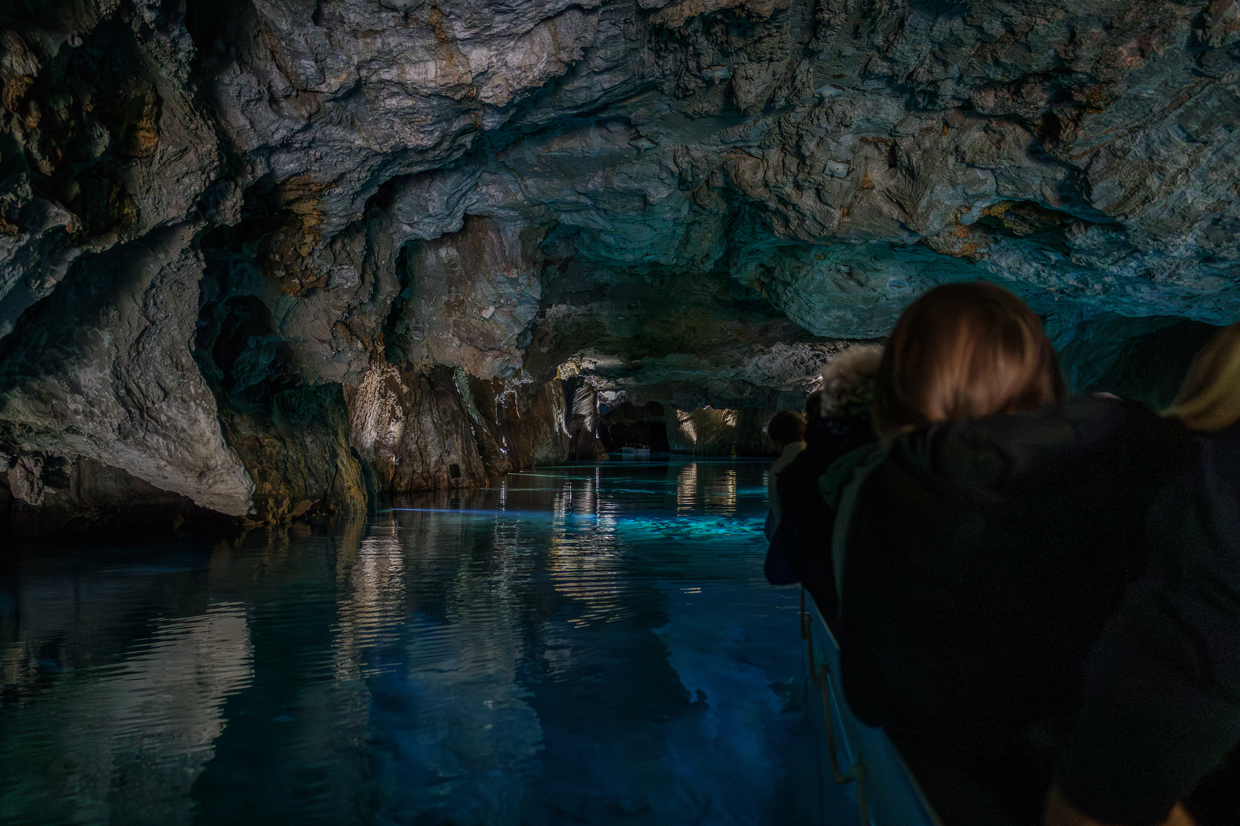 Auto-generated description: Une grotte spectaculaire aux parois rocheuses illuminées se reflète sur l'eau tandis que des gens semblent observer depuis un bateau.