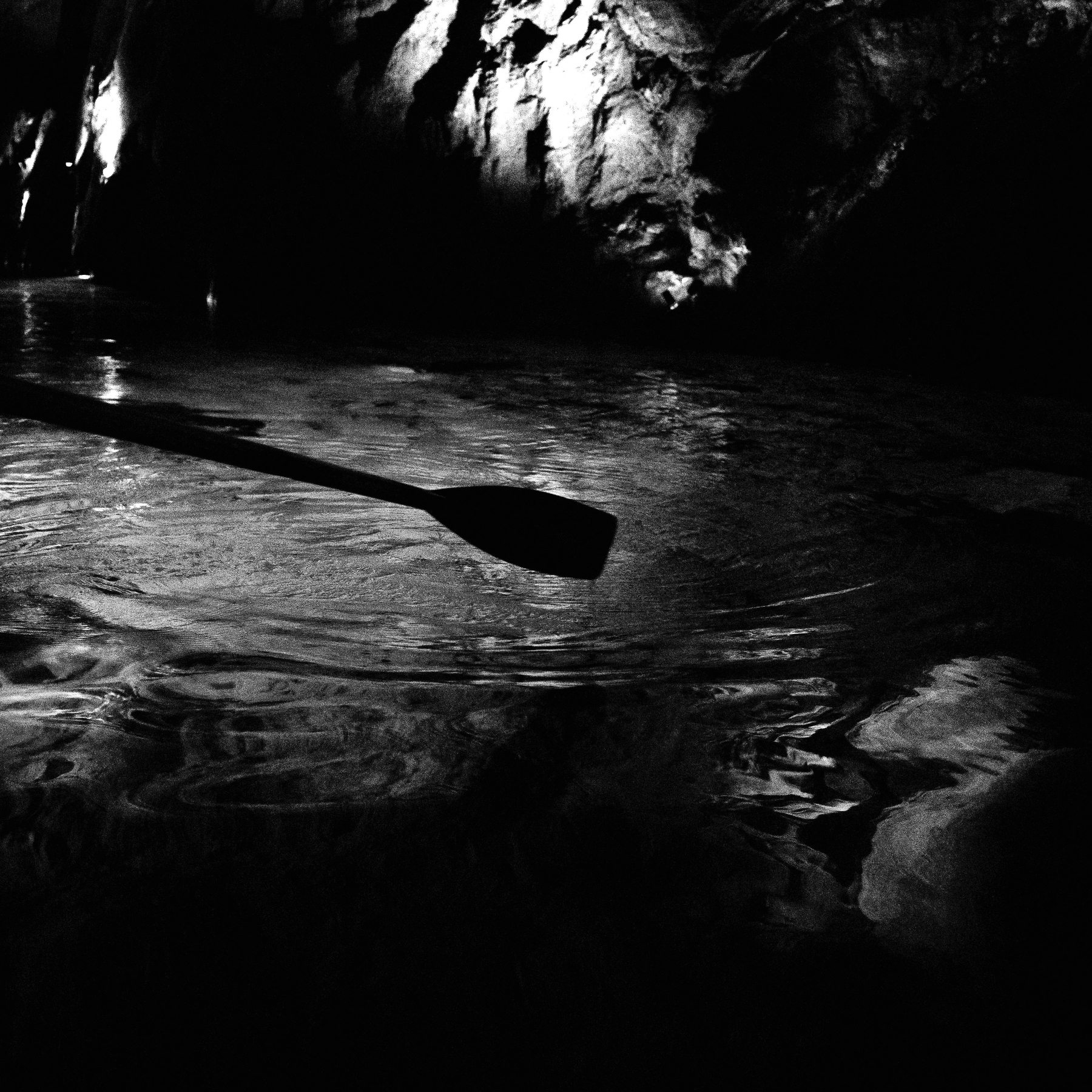 Auto-generated description: Une rame repose sur l'eau dans une scène sombre et caverneuse éclairée par une lumière douce.