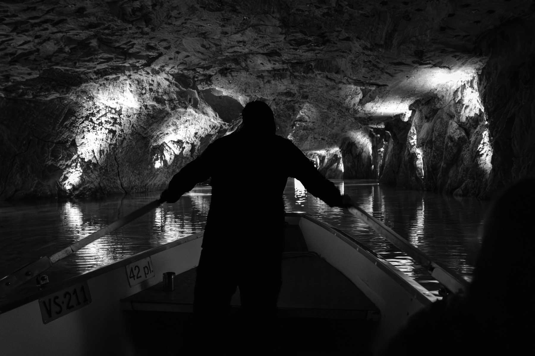 Auto-generated description: Une personne se tient debout à l'avant d'un bateau naviguant à l'intérieur d'une grotte éclairée.