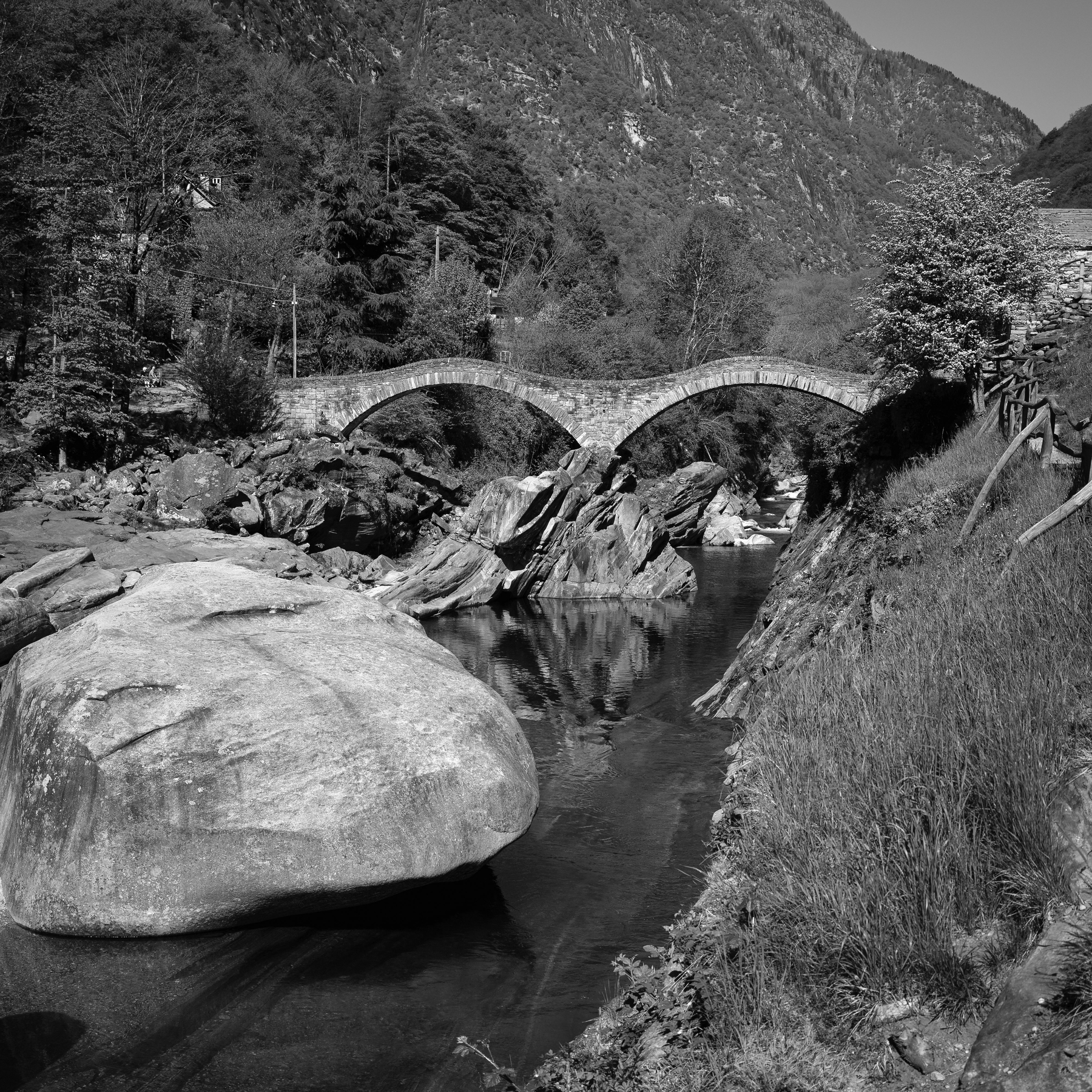 Auto-generated description: Un pont en pierre traverse une rivière entourée de rochers et de végétation montagneuse.