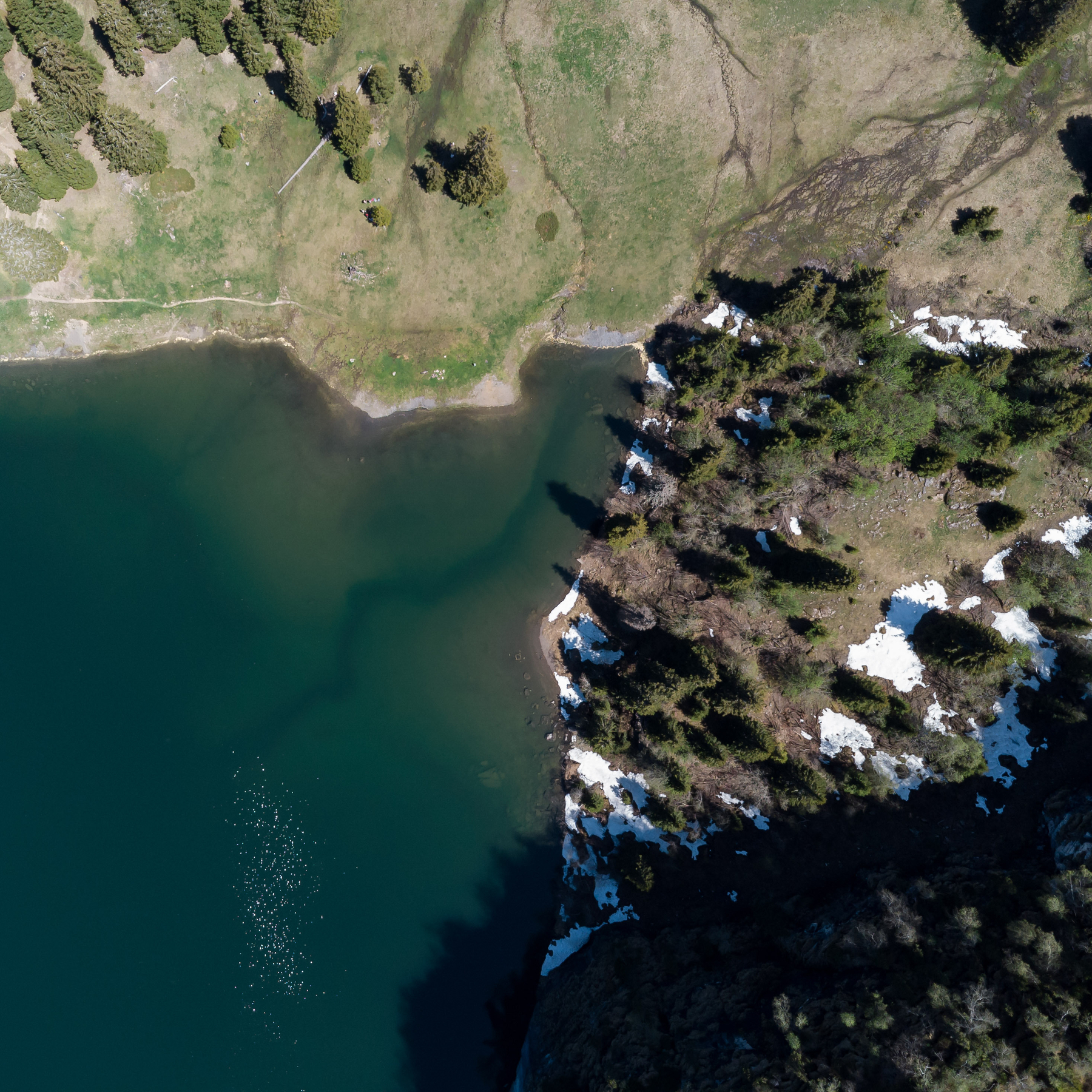 Auto-generated description: Une vue aérienne montre un lac entouré de végétation et de formations rocheuses partiellement enneigées.