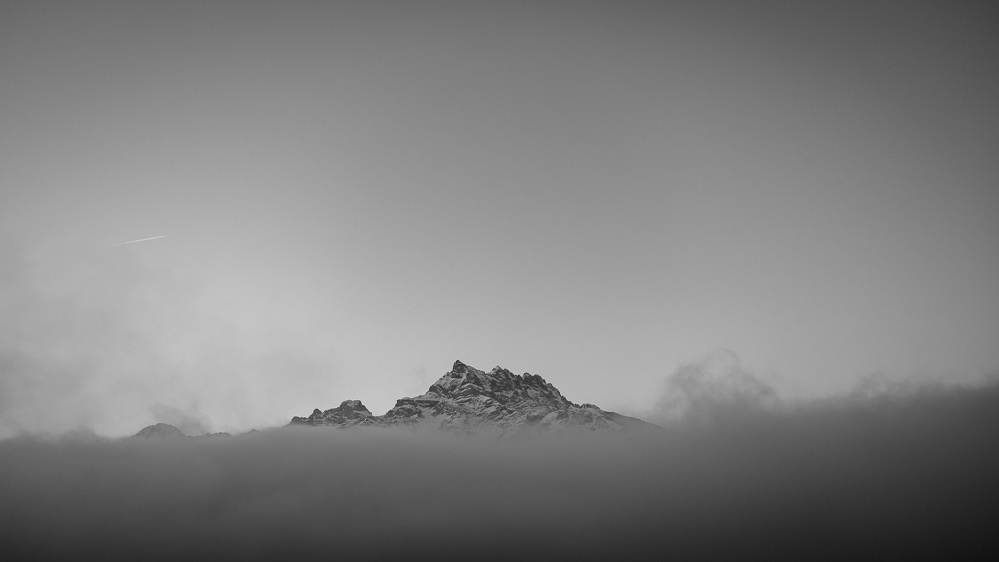 Un sommet de montagne émerge à travers un brouillard dense sous un ciel dégagé.