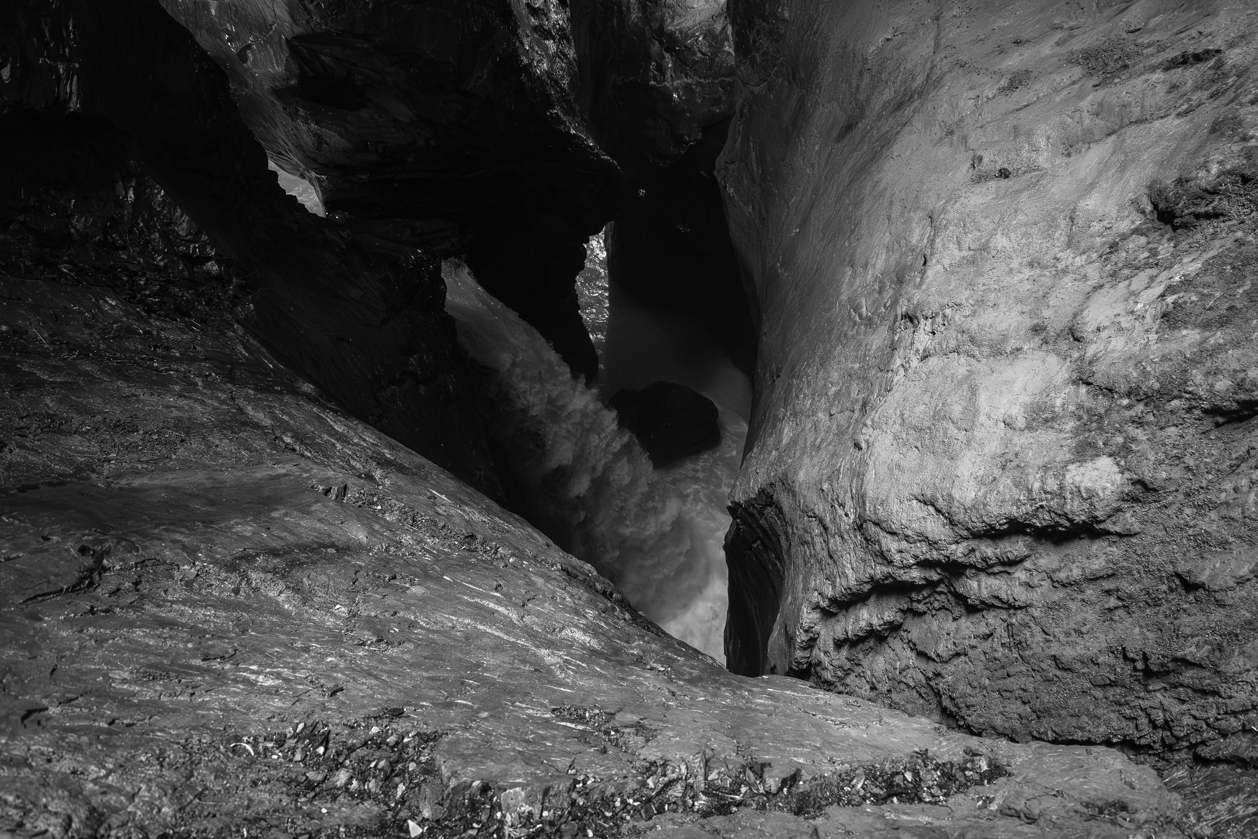 Auto-generated description: Une cascade puissante coule au milieu de rochers escarpés dans un environnement sombre et étroit.