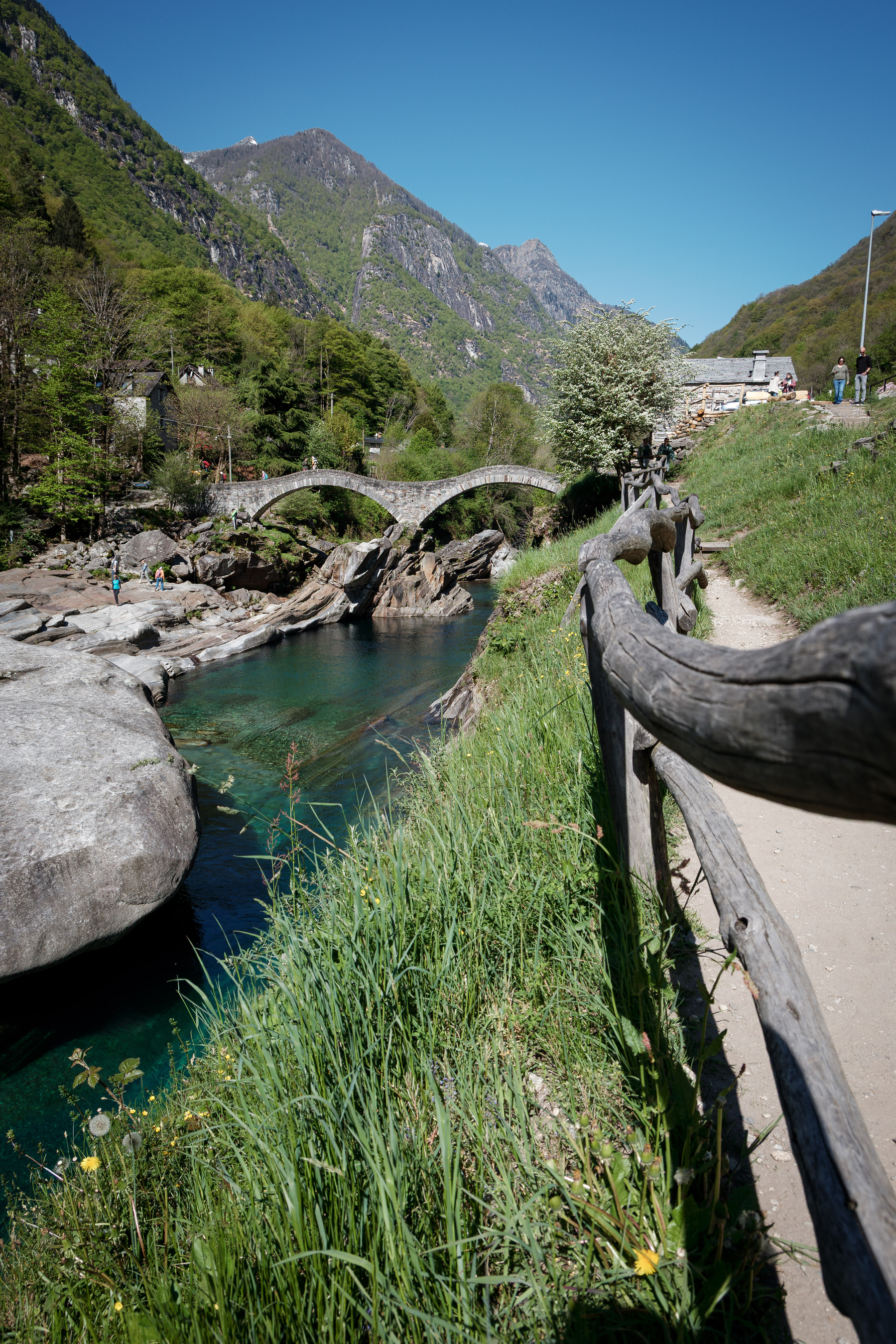 Auto-generated description: Un pont en pierre traverse une rivière entourée de collines verdoyantes sous un ciel bleu clair.