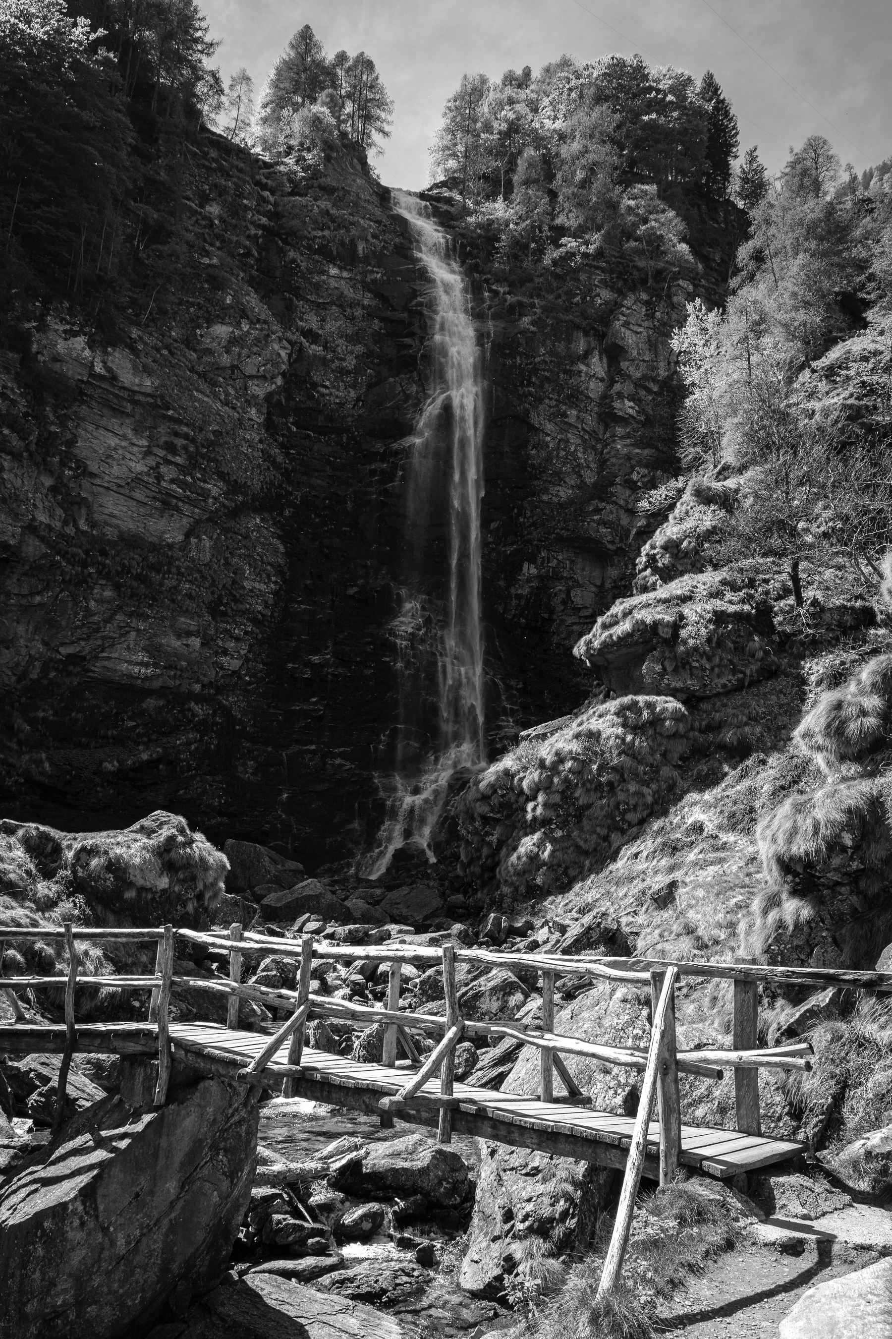 Auto-generated description: Une cascade descend d'une falaise rocheuse avec un pont en bois au premier plan.