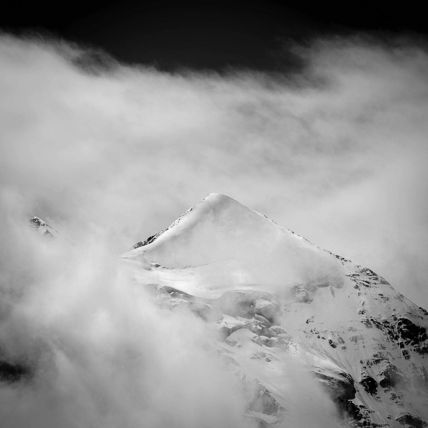 Un sommet de montagne enneigé émerge à travers des nuages épais.