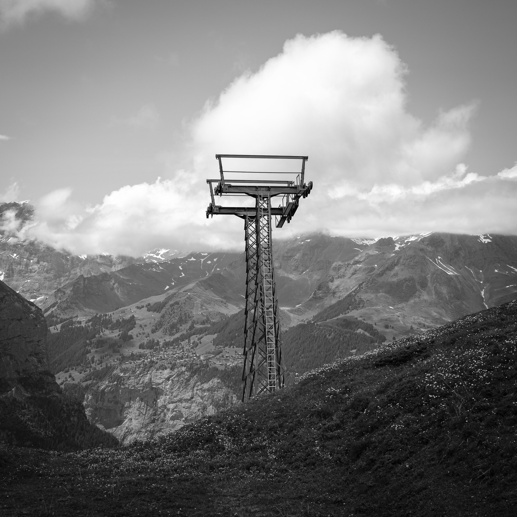 Un pylône de téléphérique se dresse devant un paysage montagneux avec des nuages dans le ciel.