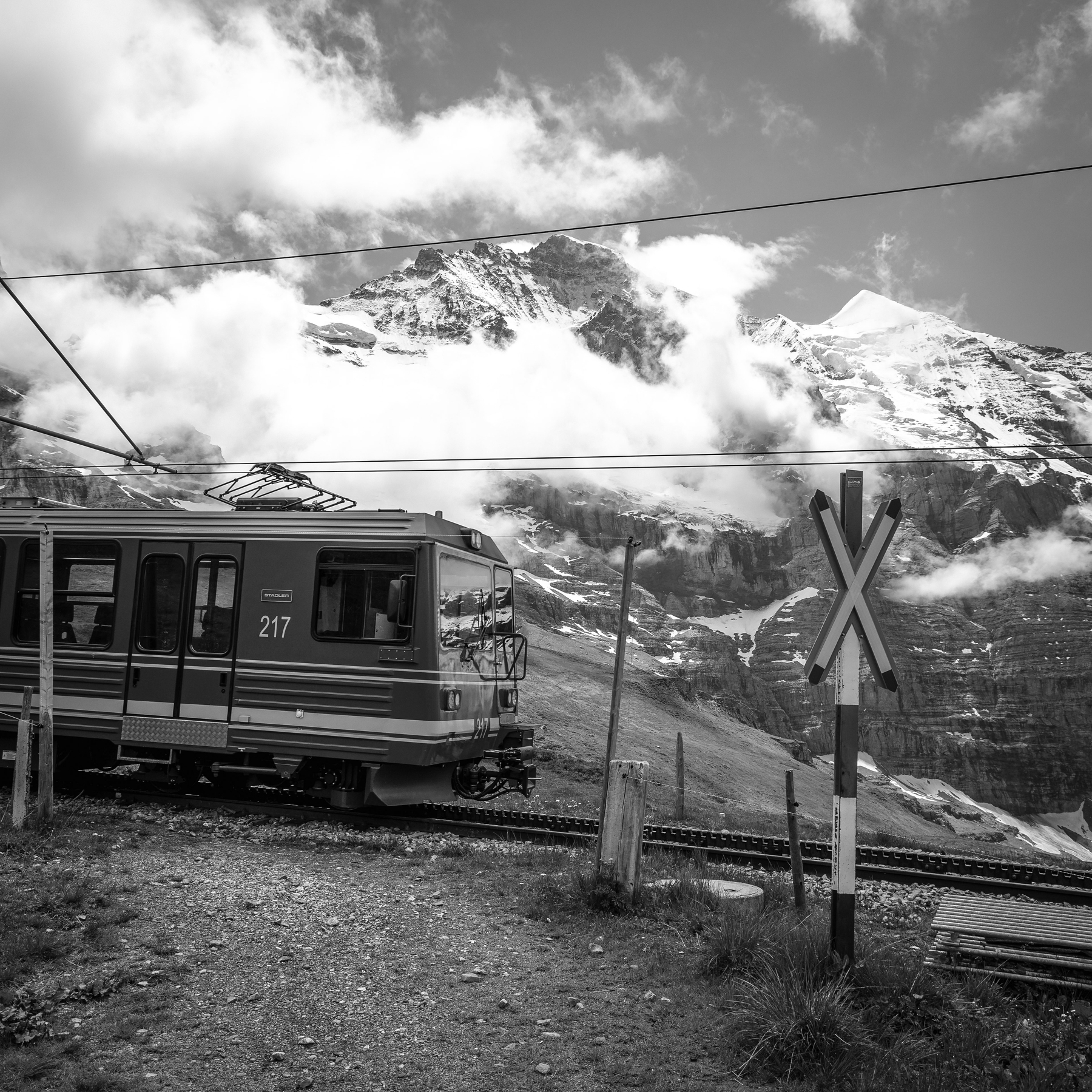 Un train de montagne traverse un paysage alpin avec des sommets enneigés en arrière-plan.