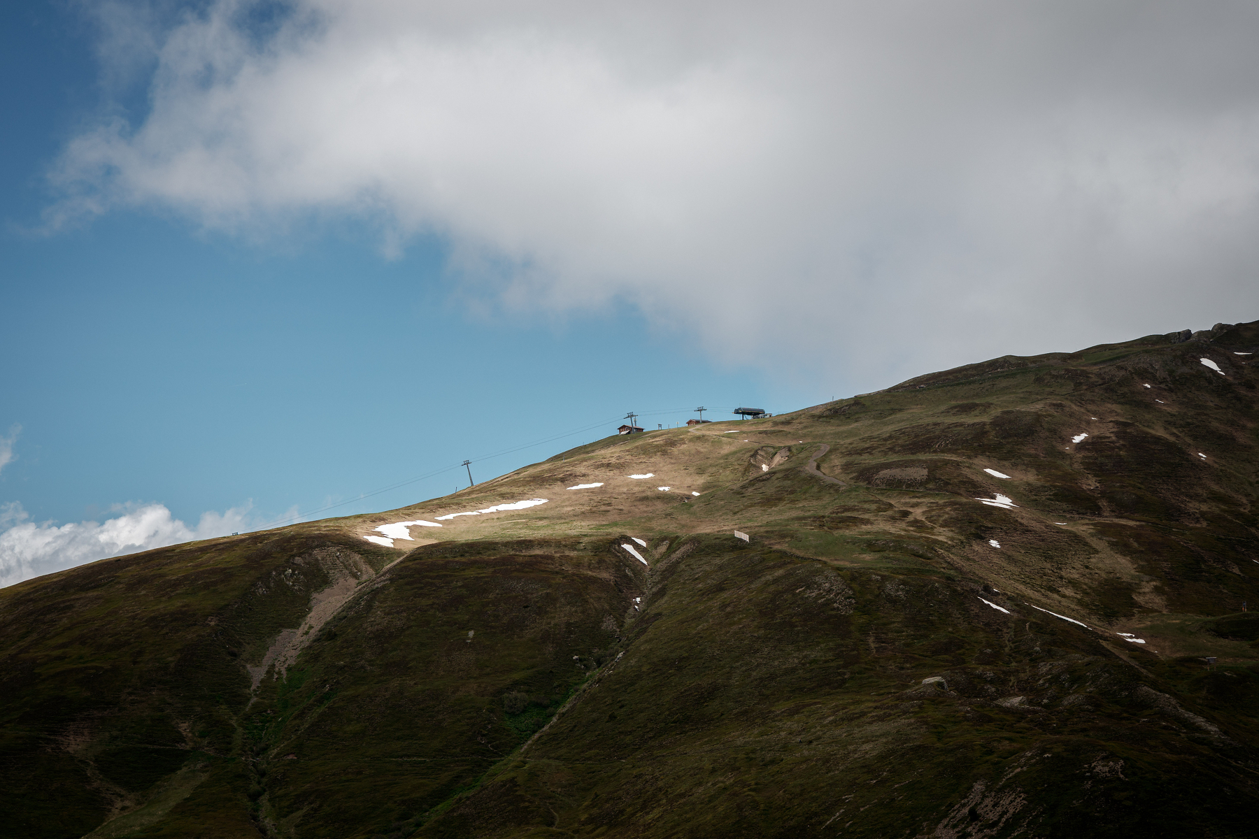 Une colline verte légèrement enneigée sous un ciel nuageux avec des structures au sommet.