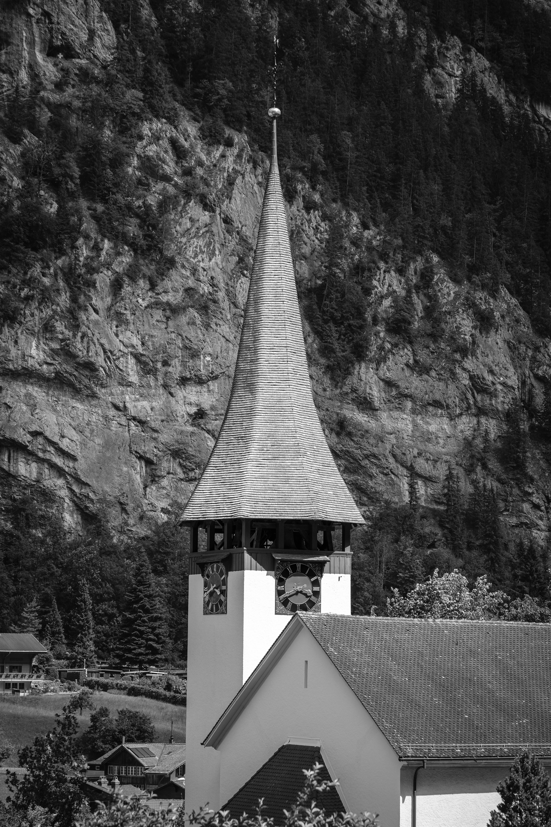 Un clocher d'église se détache sur un fond de montagnes rocheuses.