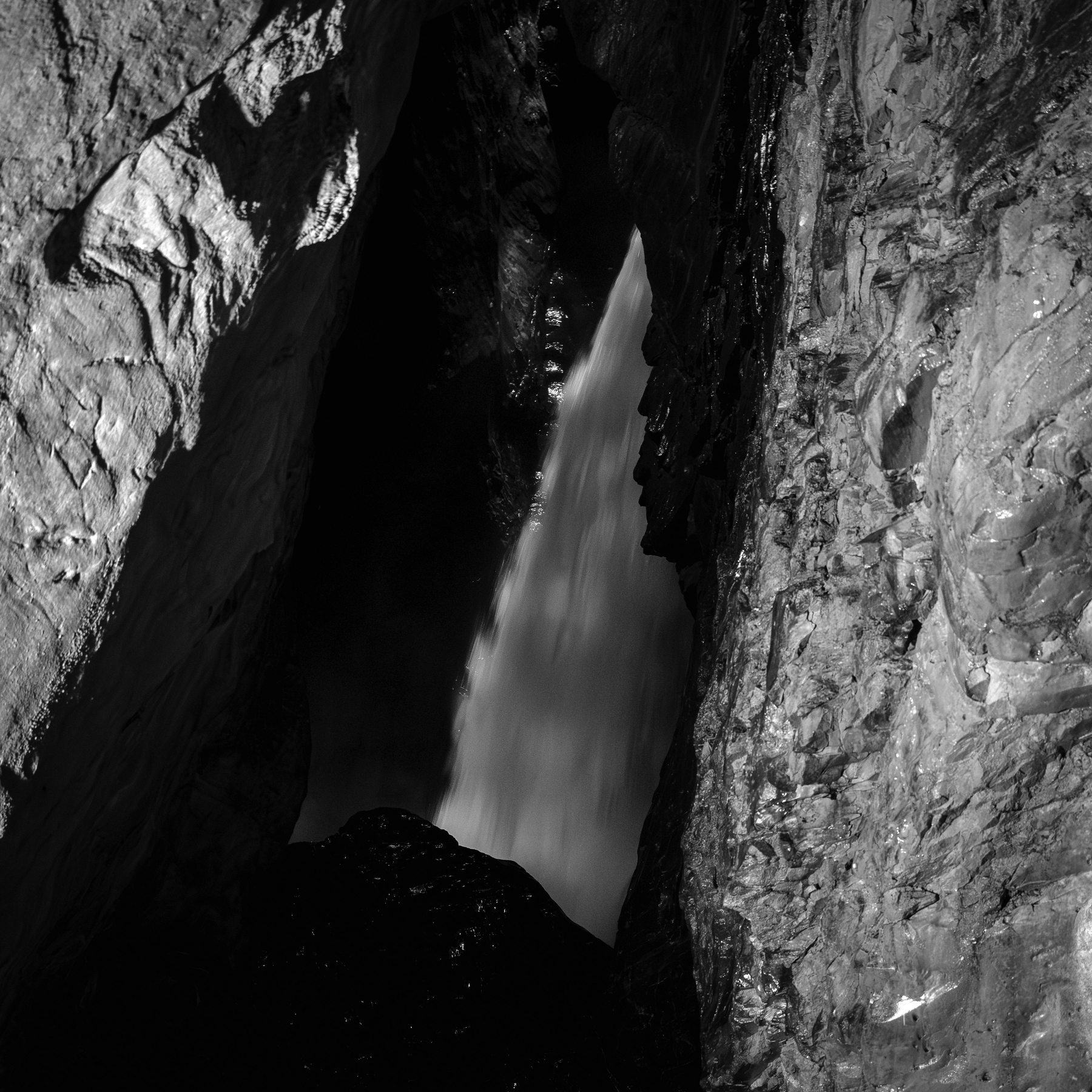 Auto-generated description: Une chute d'eau coule à travers une gorge rocheuse sombre.