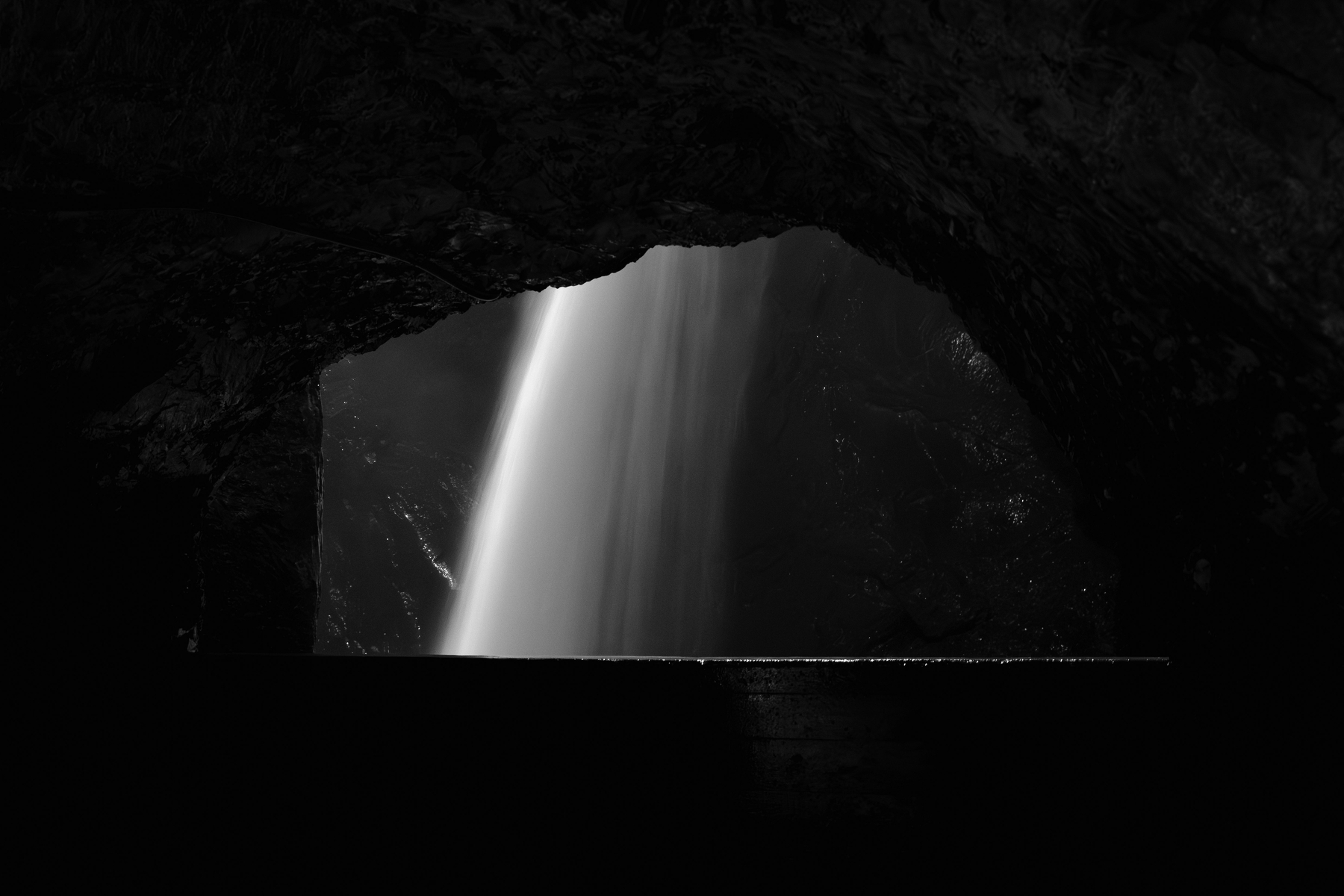 Auto-generated description: Une cascade illuminée traverse l'ouverture d'une grotte sombre.