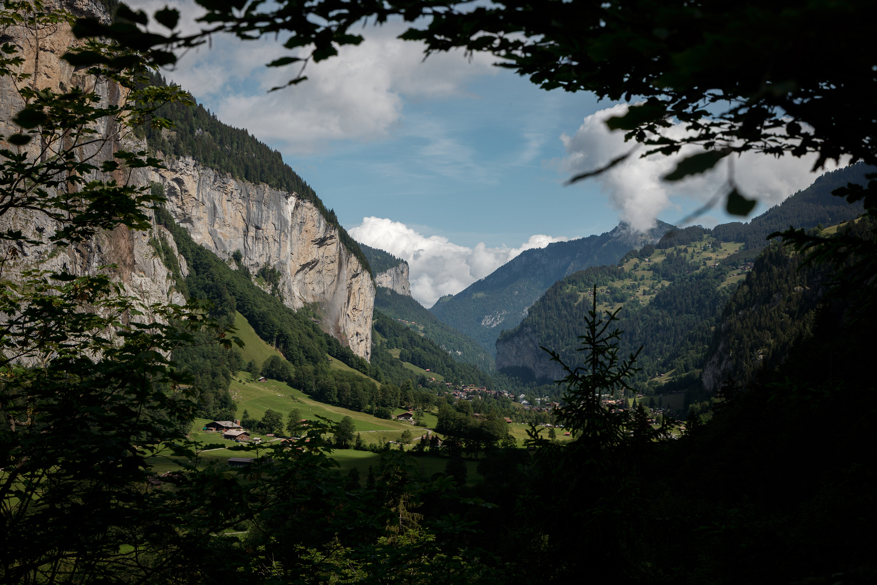 Auto-generated description: Une vallée verdoyante entourée de montagnes spectaculaires sous un ciel bleu parsemé de nuages.