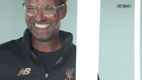 Auto-generated description: Klopp wearing glasses and a Liverpool tracksuit top is illuminated by vertical light bars.