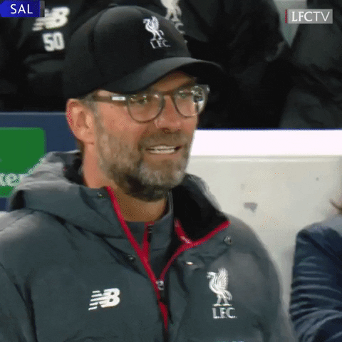 Auto-generated description: Klopp in a Liverpool FC jacket and cap is standing, appearing to react to someone or something.