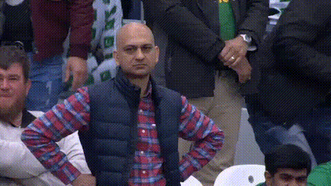 Auto-generated description: A cricket fan wearing a blue vest and red plaid shirt stands with his hands on his hips while shaking his head.