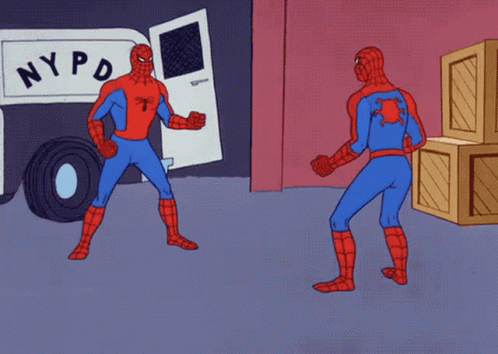 Auto-generated description: Two Spidermen are pointing at each other in confusion, with a police van and crates in the background.