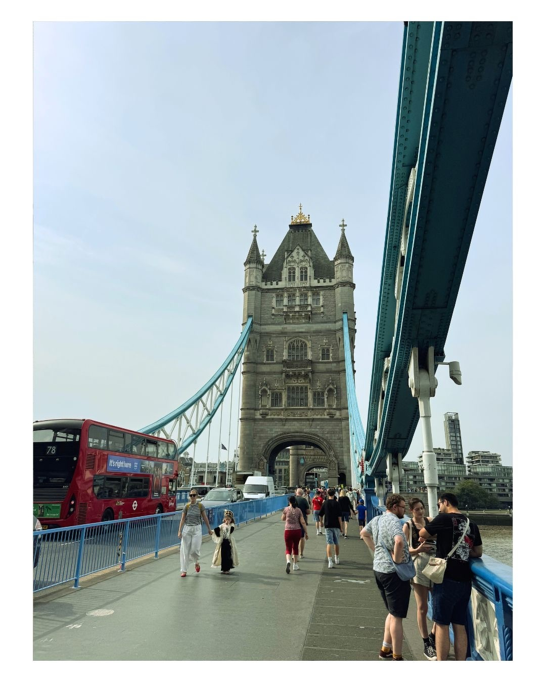 Auto-generated description: Un groupe de personnes marche et discute sur le Tower Bridge à Londres, avec un bus rouge circulant à côté.
